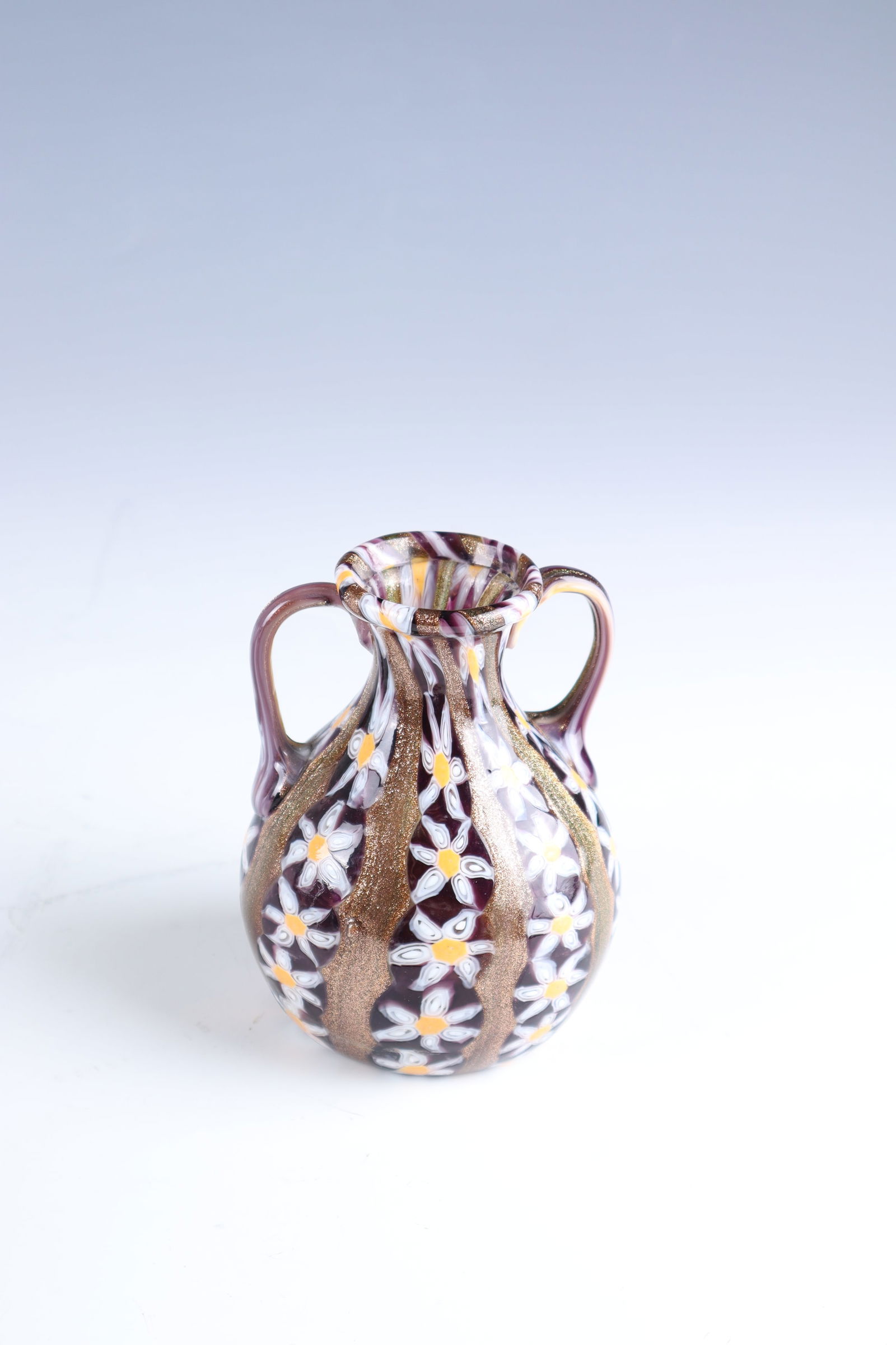 Henkelvase ''A Murrine Floreali'': Henkelvase ''A Murrine Floreali'' Fratelli Toso, Murano, c. 1910 Colourless glass. Vertical ribbon fusion in aventurine and violet with floral murrine. Surface acid-polished. H. 10.3 cm.