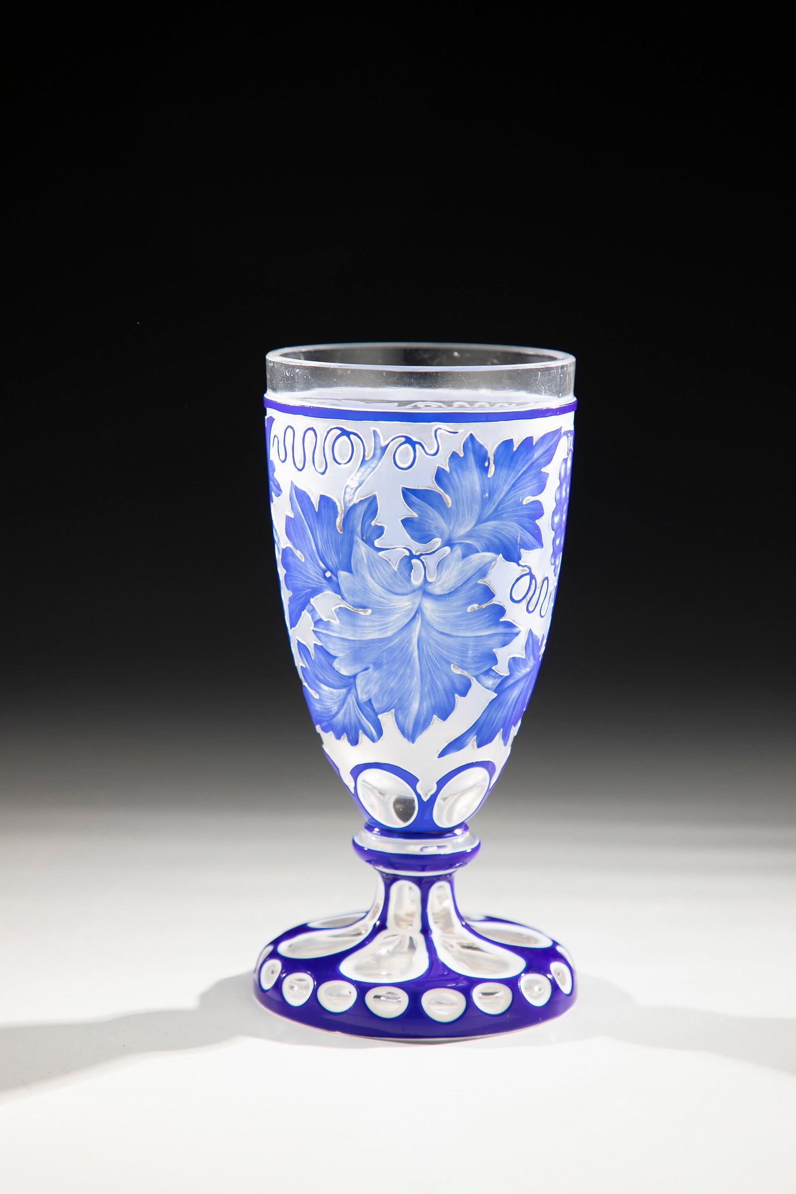 Foot cup with double overlay: Foot cup with double overlay North Bohemia, c. 1860 Colourless, first white, then cobalt blue overlaid glass, decorated in layered engraving with vine tendrils and grapes. H. 15.5 cm