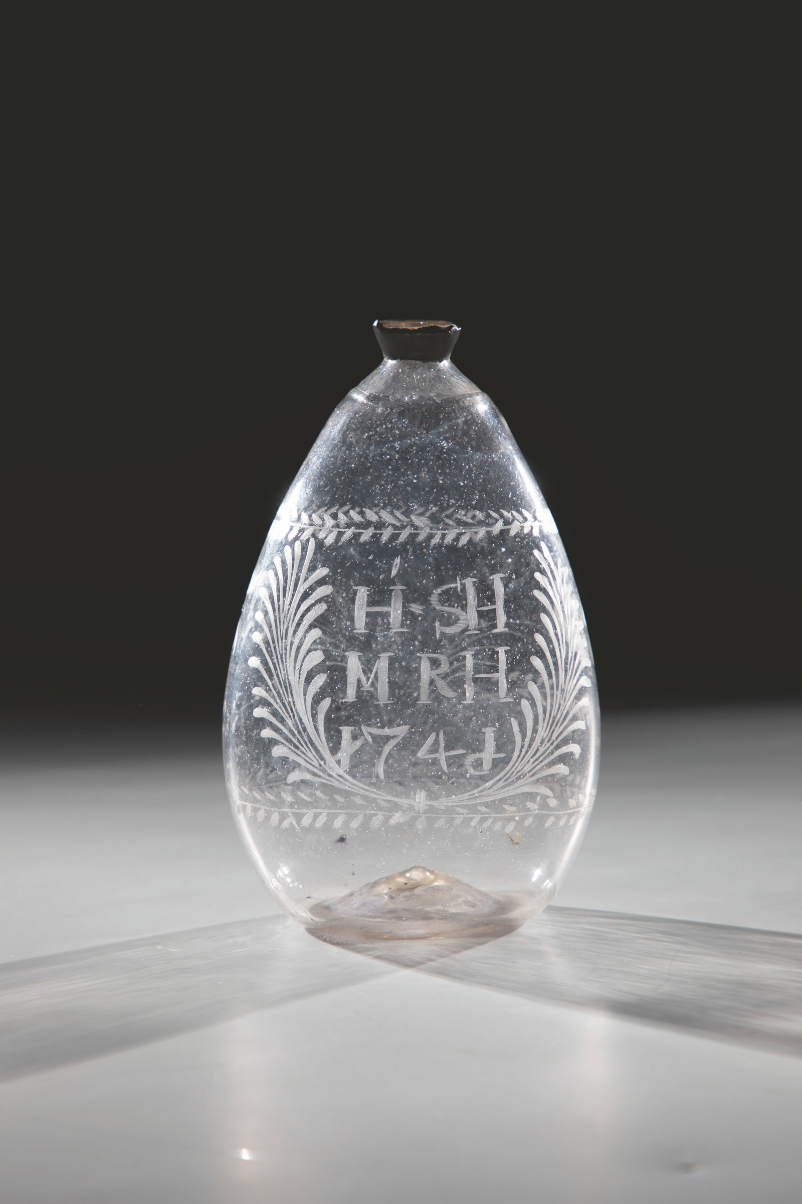 Pouch bottle: Bag bottle Alpine, dated 1746 Slightly greyish glass with tear-off. Slightly raised floor. Initials engraved on the front by crossed palm branches and date: ''H. SH / M RH / 1746''. Stylized flower bu
