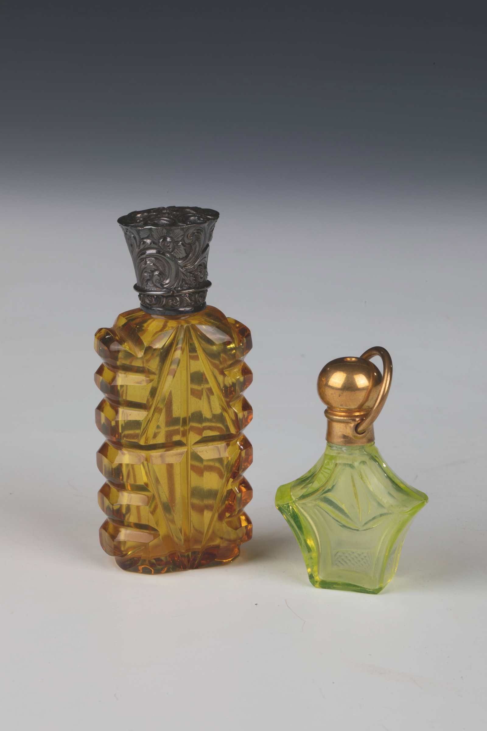 Two miniature bottles: Two miniature flacons 19th/20th century Yellow glass and light green uranium glass, faceted and reliefed respectively. With original, finely reliefed silver or gilded screw and hinge covers. H.5.5-8.5