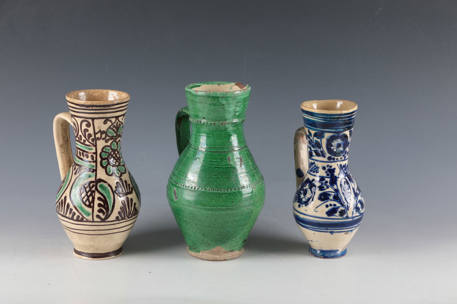 Three Jugs: Three jugs of Transylvania, Alzen, Hammersdorf, 19th and 20th centuries Stylised floral décor on a butter-coloured background in brown, green and blue as well as green glazed with fluted décor and r