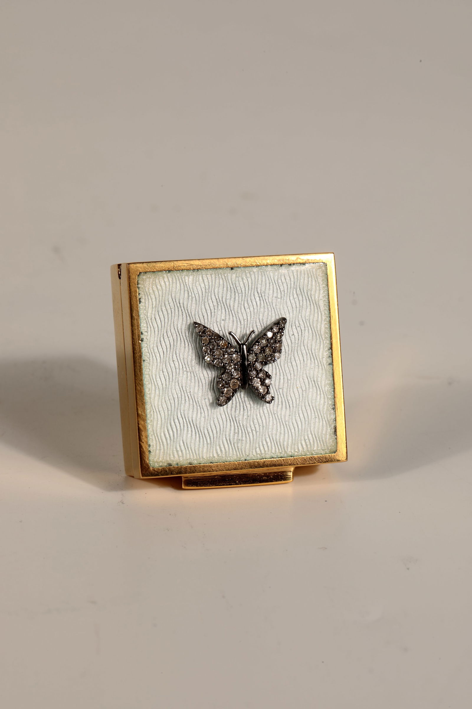 Small tin: Small tin Square pill box with hinged lid, white enamel over guilloché wave decoration. In the middle a small butterfly with wings studded with octagonal diamonds. approx. 0.20 ct. Silver gold-plated