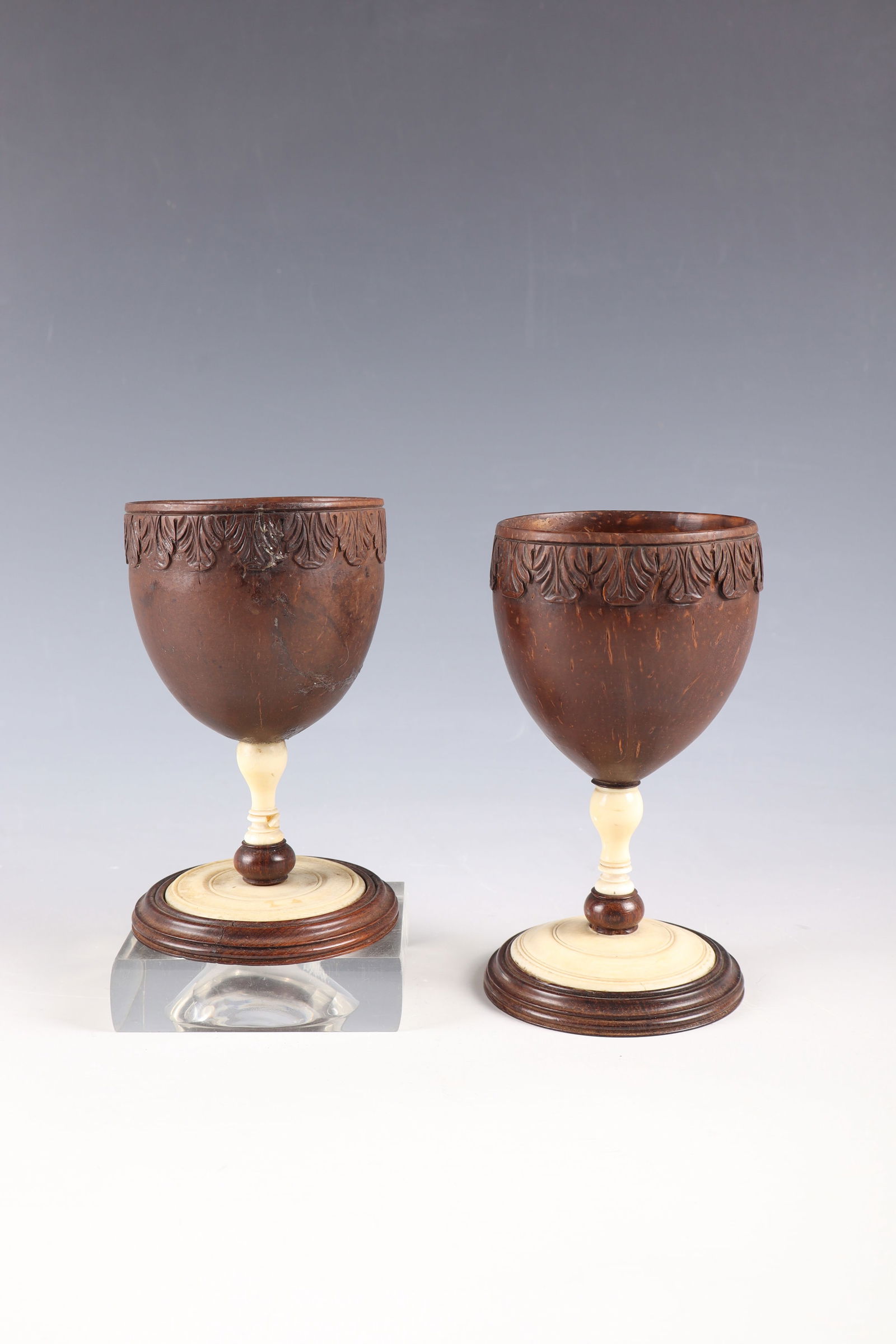 Two coconut cups: Two coconut goblets, 18th / 19th century, endocarp. Baluster shaft turned, lip rim with carved acanthus leaf decoration. One part damaged and glued. H. 12.5-14 cm
