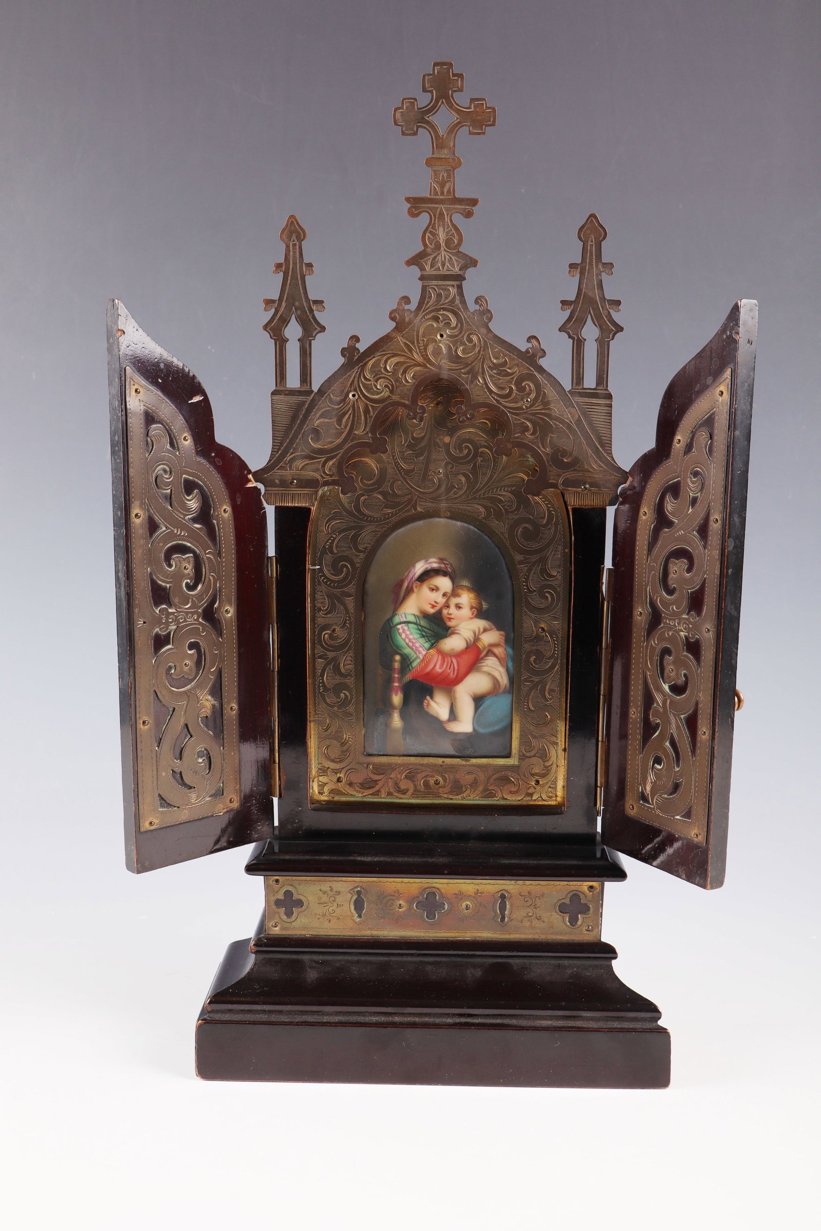 House altar with porcelain painting ''Madonna della Sedia'': House altar with porcelain painting ''Madonna della Sedia'' Italy, end of the 19th century Dark brown wood and sheet brass, ornamentally pierced and engraved, 2-door middle section with polychrome pai