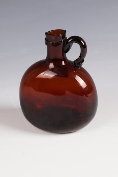 Bocksbeutel with handle: Bocksbeutel with handle Franken, 18th century. Brown glass with tear-off. Bulbous body flattened on both sides. Short tubular neck with appliquéd handle and applied glass band. H. 13 cm Cf. Lit.: