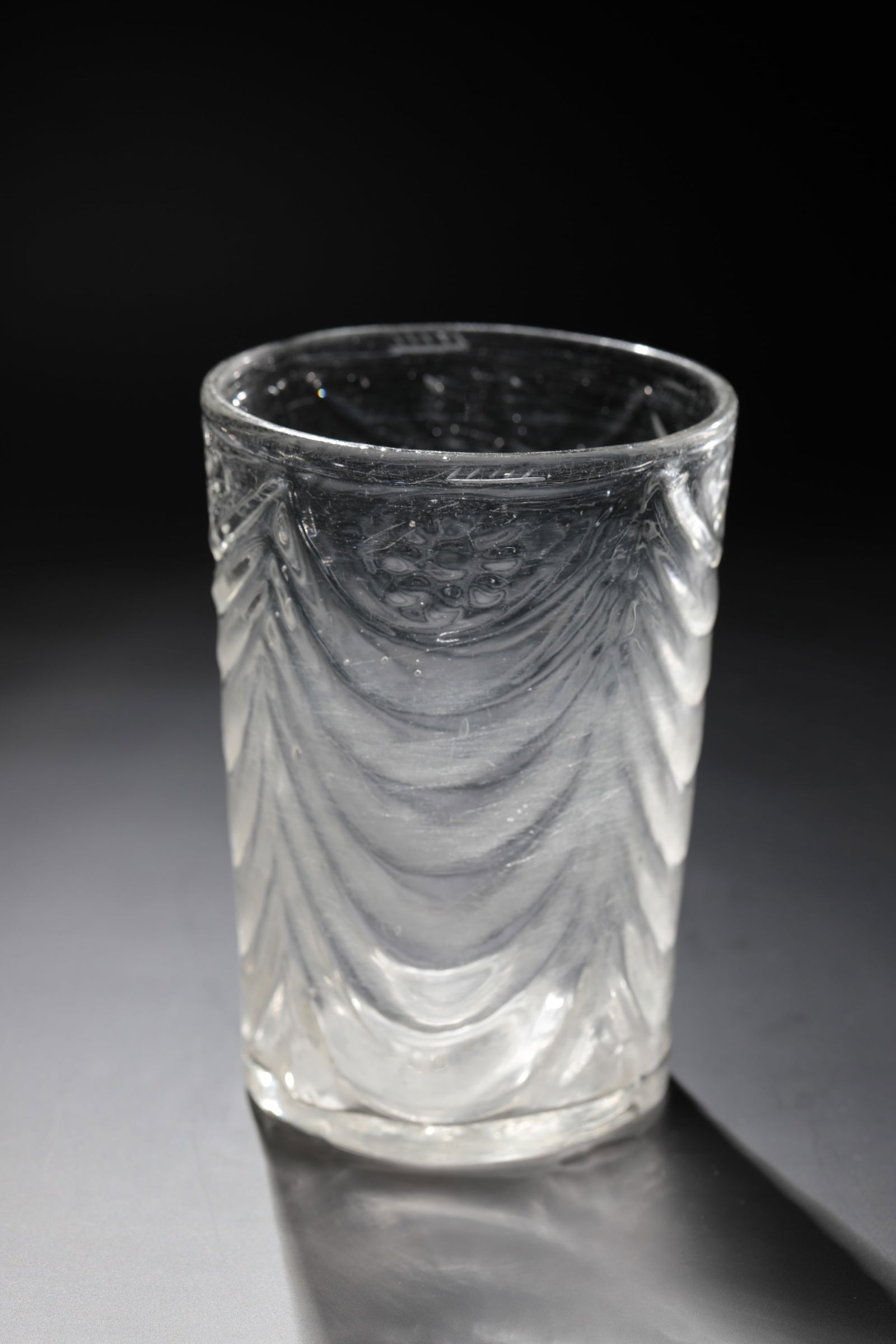 Dispensing cup: Beer cup Southern Germany or Austria, 18th century Colourless, mould-blown glass with hanging ornaments and flowers in quadruple repeat. Coal Inclusions. Below the lip edge, engraved calibration line.