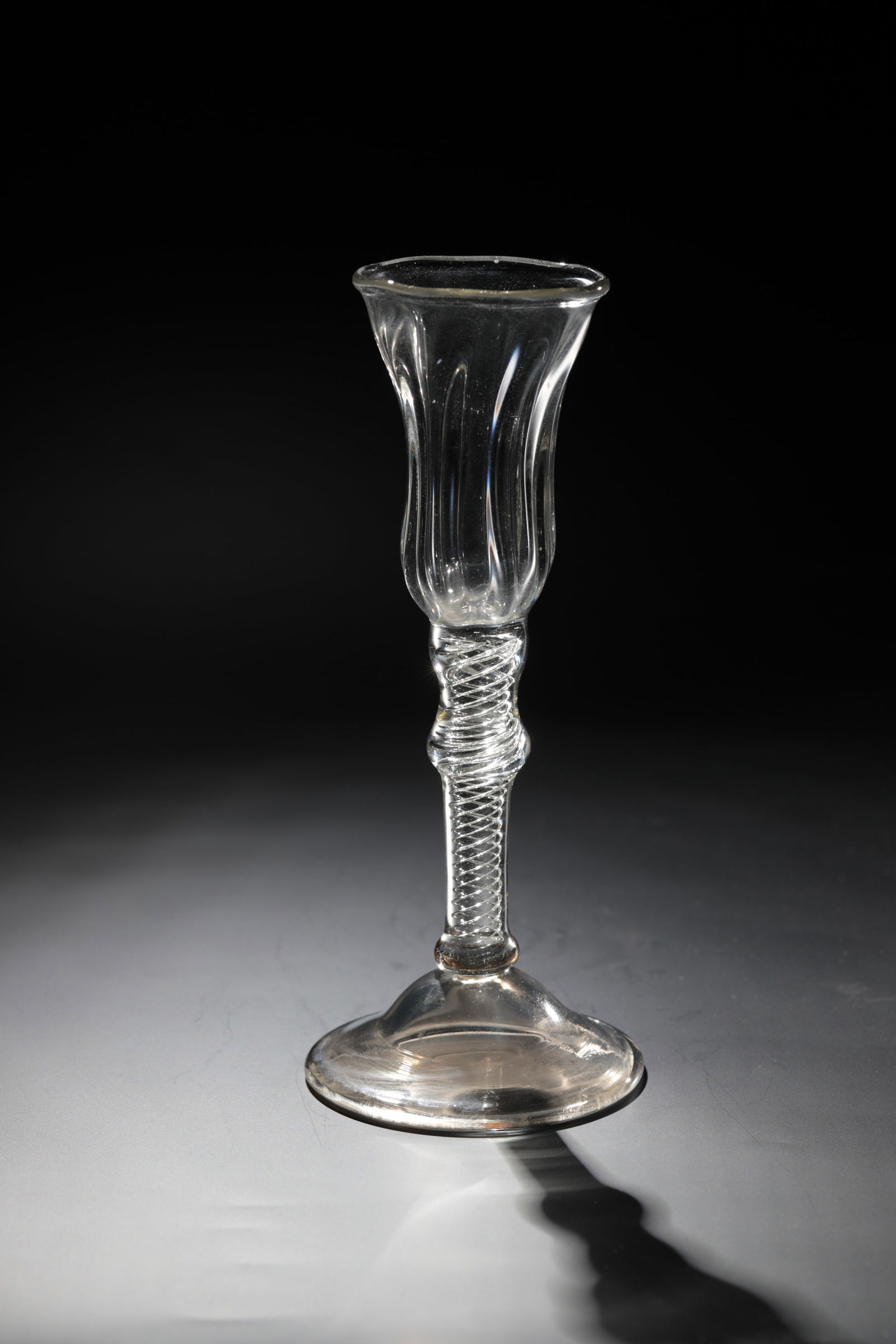 Filament glass: Thread glass, England, 18th / 19th century. Slightly rising disc base greyish. Baluster shaft with spiral hollow threads and ribbed, bell-shaped cuppa made of colourless glass. H. 19.5 cm