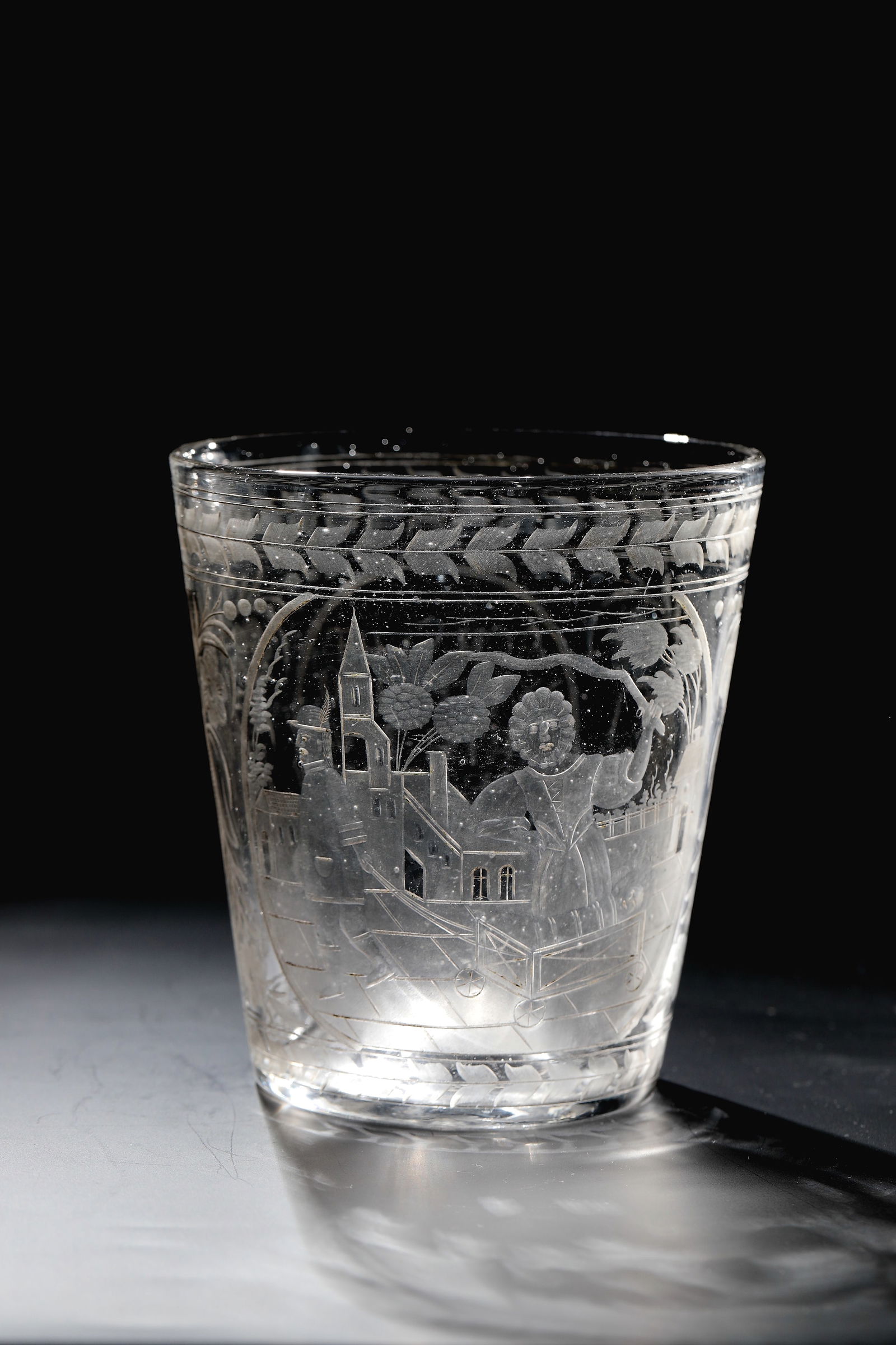Joke cup: Joke cup Brandenburg or Saxony, around 1700 Colourless glass with tear and raised bottom. On the slightly conically widened wall, deep-engraved scene and inscription. Frontal with allegorical
