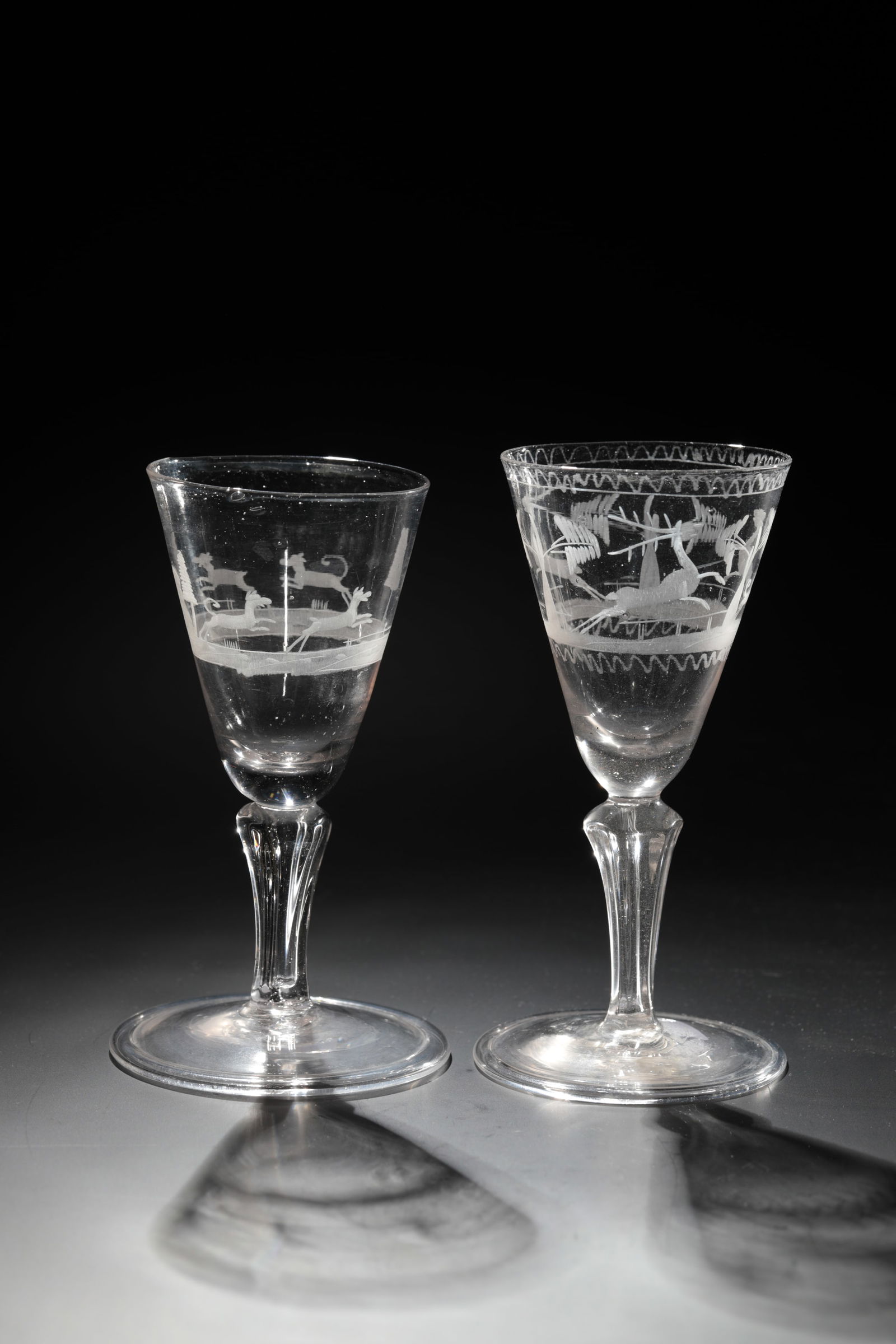 Two hunting cups: Two hunting goblets Thuringia, 18th century Colourless glass with tear-off. Disc base with the edge folded downwards. Pseudo-faceted baluster shaft. Hunting scene cut on the conically widened kuppa: