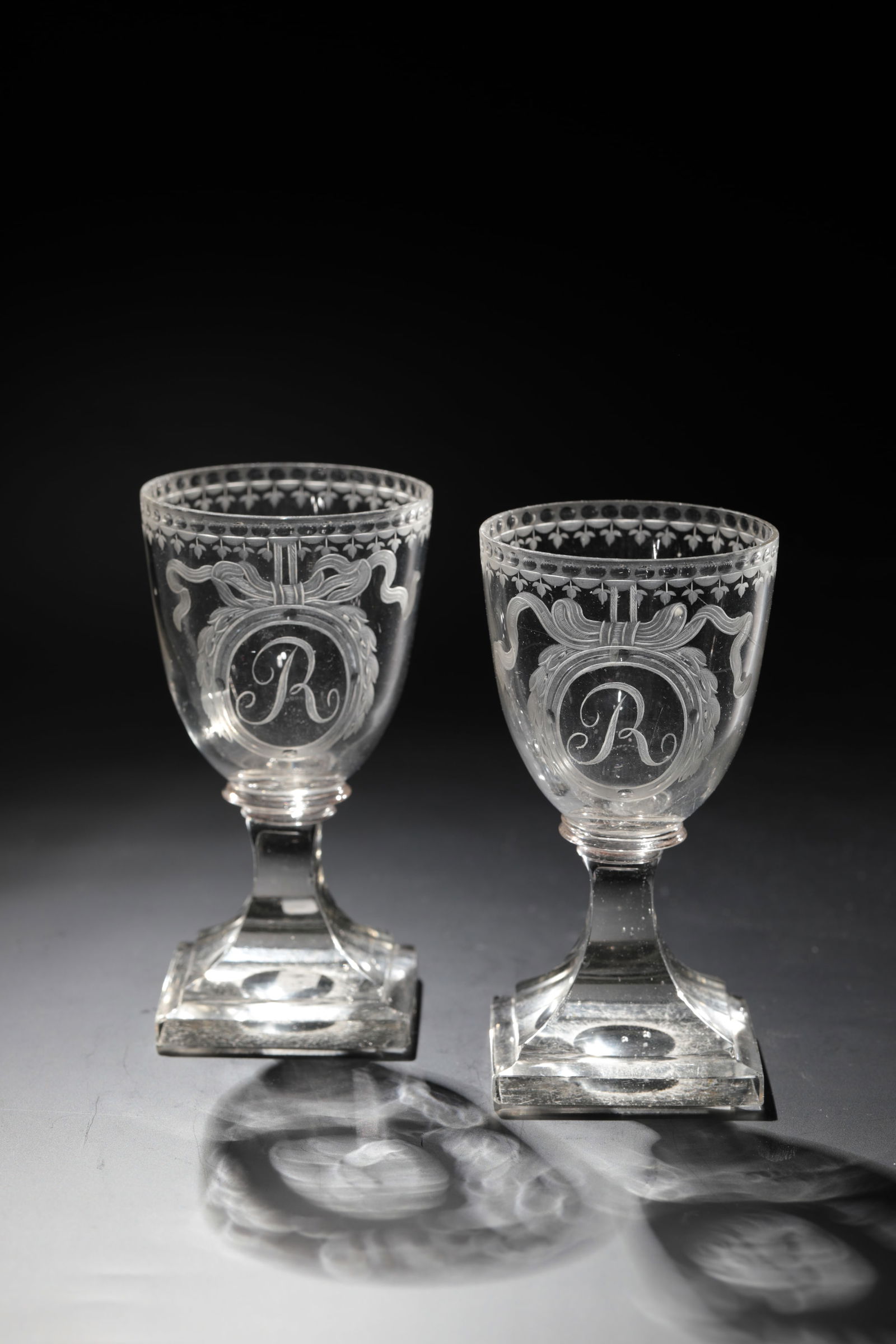 Pair of Empire Goblets: Pair of Empire Goblets, North German, circa 1815, Colorless glass. Square plinth chipped with bottom ball. Peeled shaft. Letter ''R'' cut frontally on an egg-shaped cuppa in an oval medallion. Lip