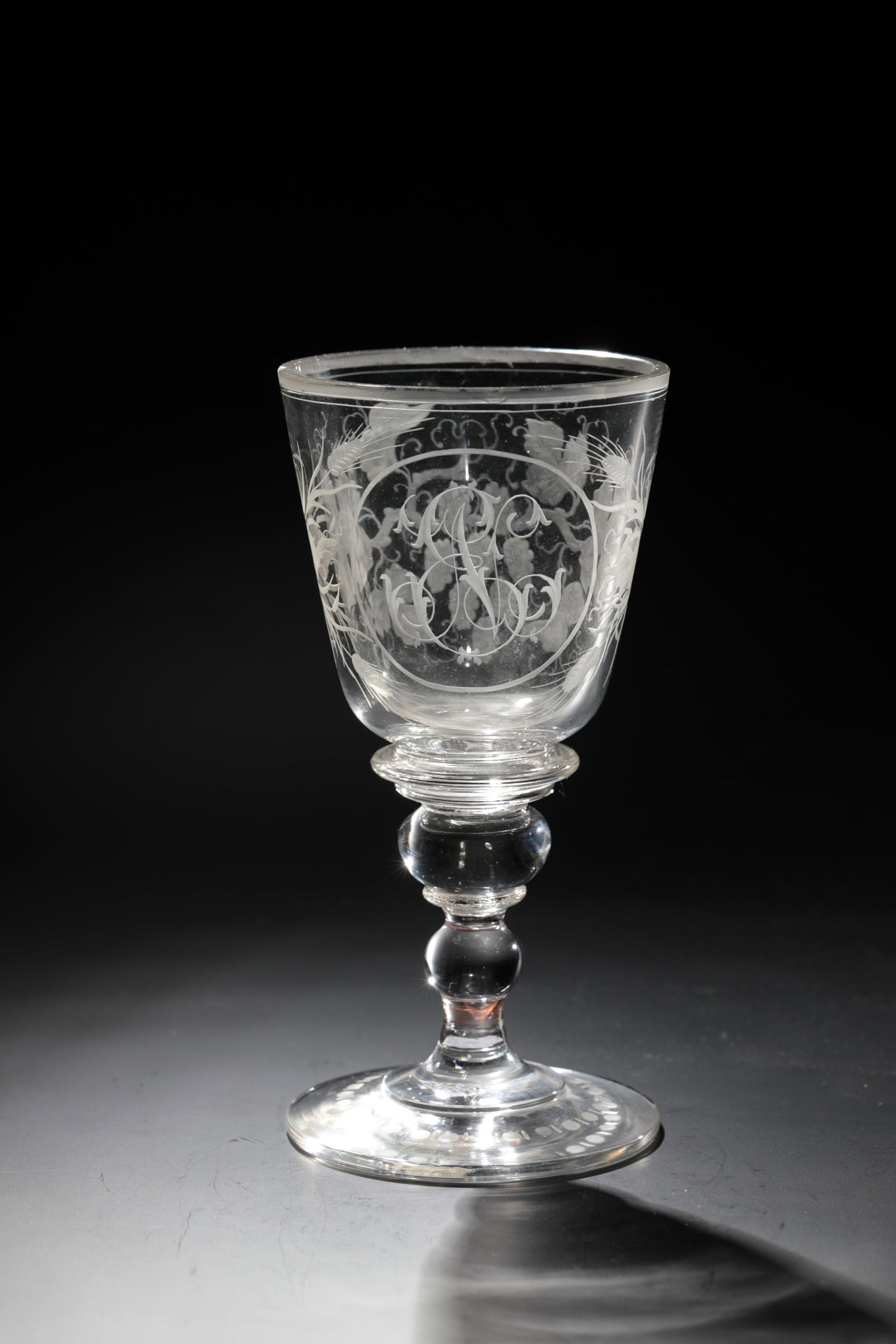 Cup: Goblet Bohemia, 19th century Colourless glass. Disc base, baluster shaft with ball nodus. Frontal on the Kuppa initials ''EN'' surrounded by vines and ears of corn. Matt lip edge chipped. H. 18.5 cm