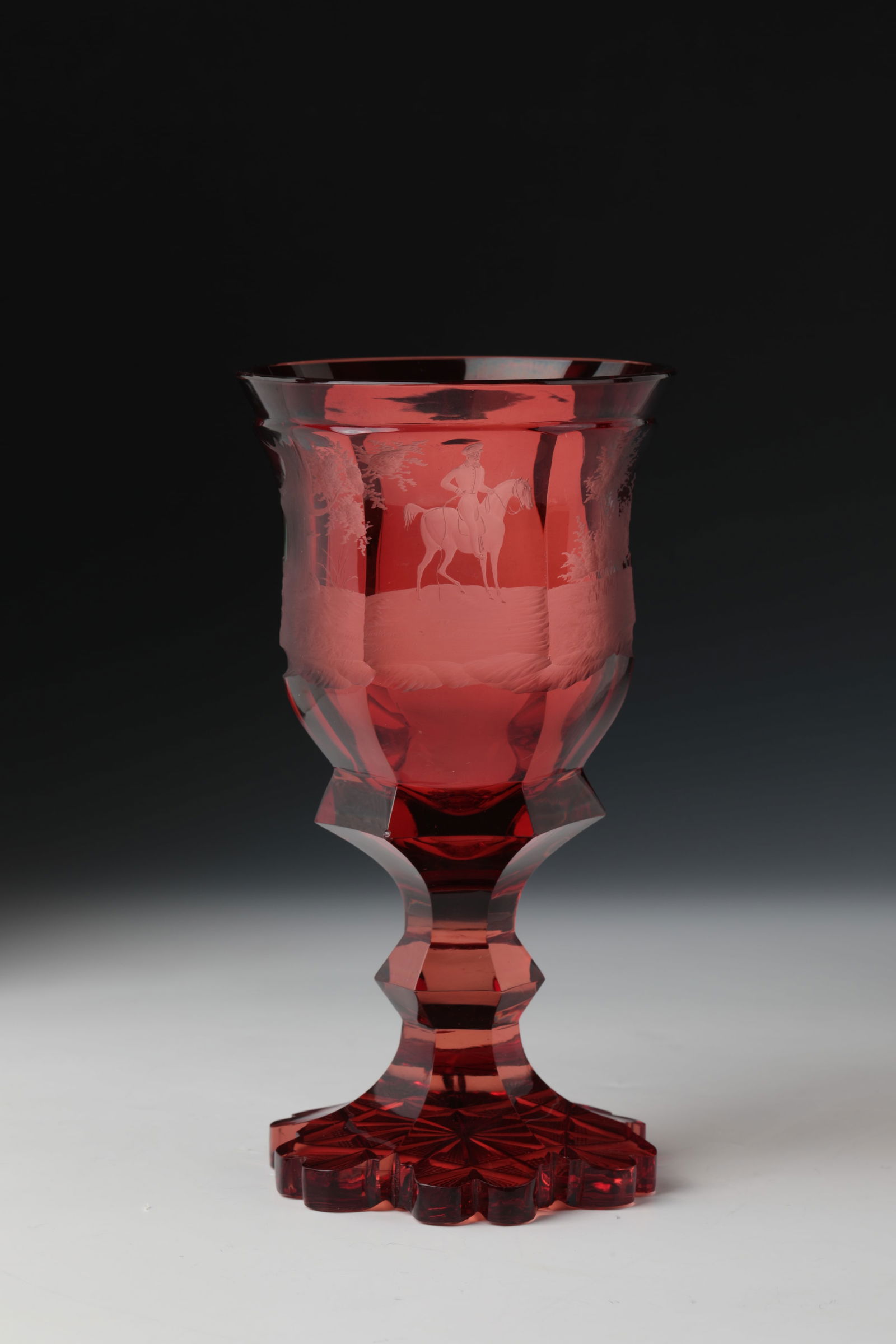 Cup: Goblet Bohemia, c. 1840 Colourless, ruby-red glazed glass. Fitted foot with polished back. Faceted shaft with nodus. On the faceted, bell-shaped wall, finely cut hunting scene all around: in front of