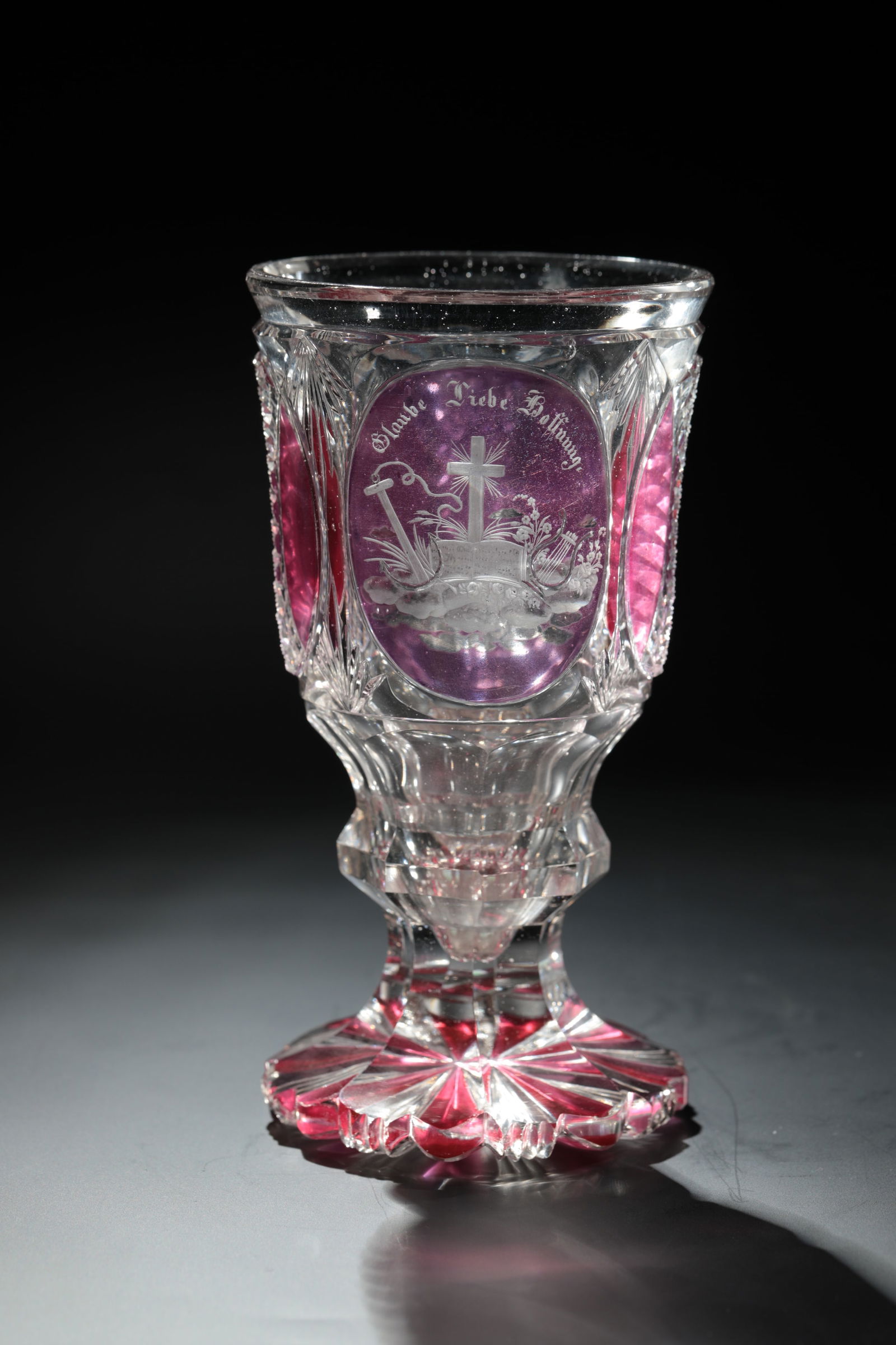 Goblet with allegories: Goblet with allegories of North Bohemia around 1840 Colourless glass, partially with pink and violet glaze. Cutely ground foot with notched and roller cut decoration. Faceted shaft, frontal on the