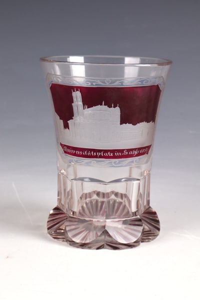 Mug: Beaker Bohemia, c. 1845 Colourless, partly purple glazed glass. Faceted foot with notched bottom and faceted wall base. Frontal view cut into rectangular field in: ''Universitätsplatz in Salzburg''.