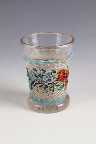Pearl Ribbon Cup: Pearl Ribbon Beaker North Bohemia, c. 1830 Grey-tinted glass with notched star on the underside. Body with polychrome, fine beading: floral tendrils between serrated borders. Defects. H. 11 cm