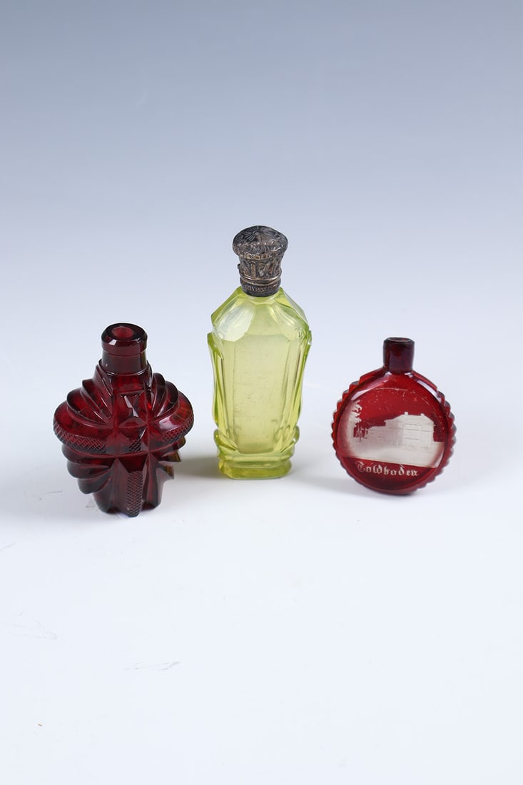 Three miniature bottles: Three miniature bottles Bohemia, mid-19th century AnnaYellow uranium glass, cut-decorated, with metal cap. H. 9 cm. Colourless, red glazed glass with cut and marked view. H. 5.5 cm. Red, richly cut