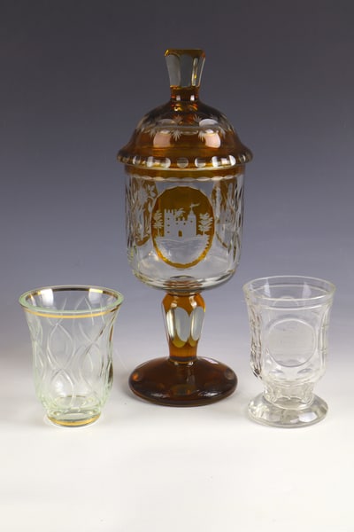 Large lidded cup, foot cup and mug: Large lidded goblet, foot cup and cup Bohemia, 2nd half of the 19th century. Lidded goblet: colourless, partly amber-coloured, cut-decorated glass with three oval medallions, in which cut representati