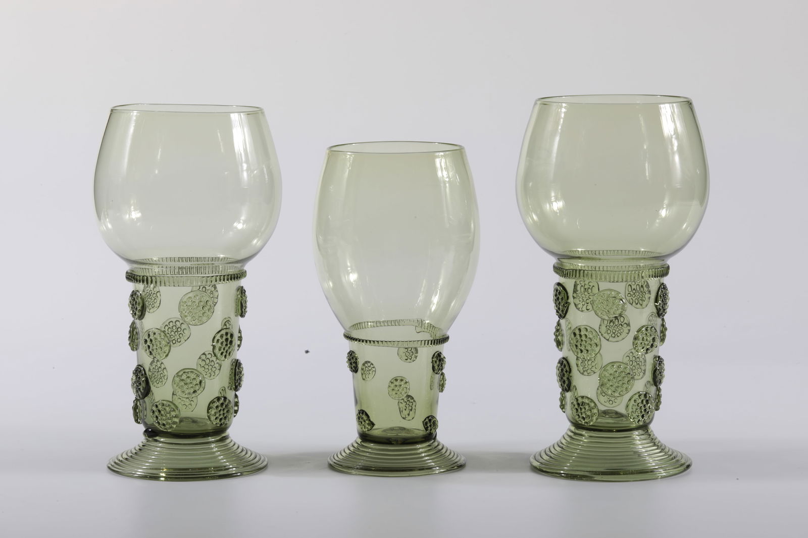 Three Romans: Drei Römer Rheinische Glashütten AG, Cologne-Ehrenfeld, around 1881 Olive-coloured glass. Decorated all around with nubs, spun foot. H: 20.5 cm / 20 cm / 17.5 cm.