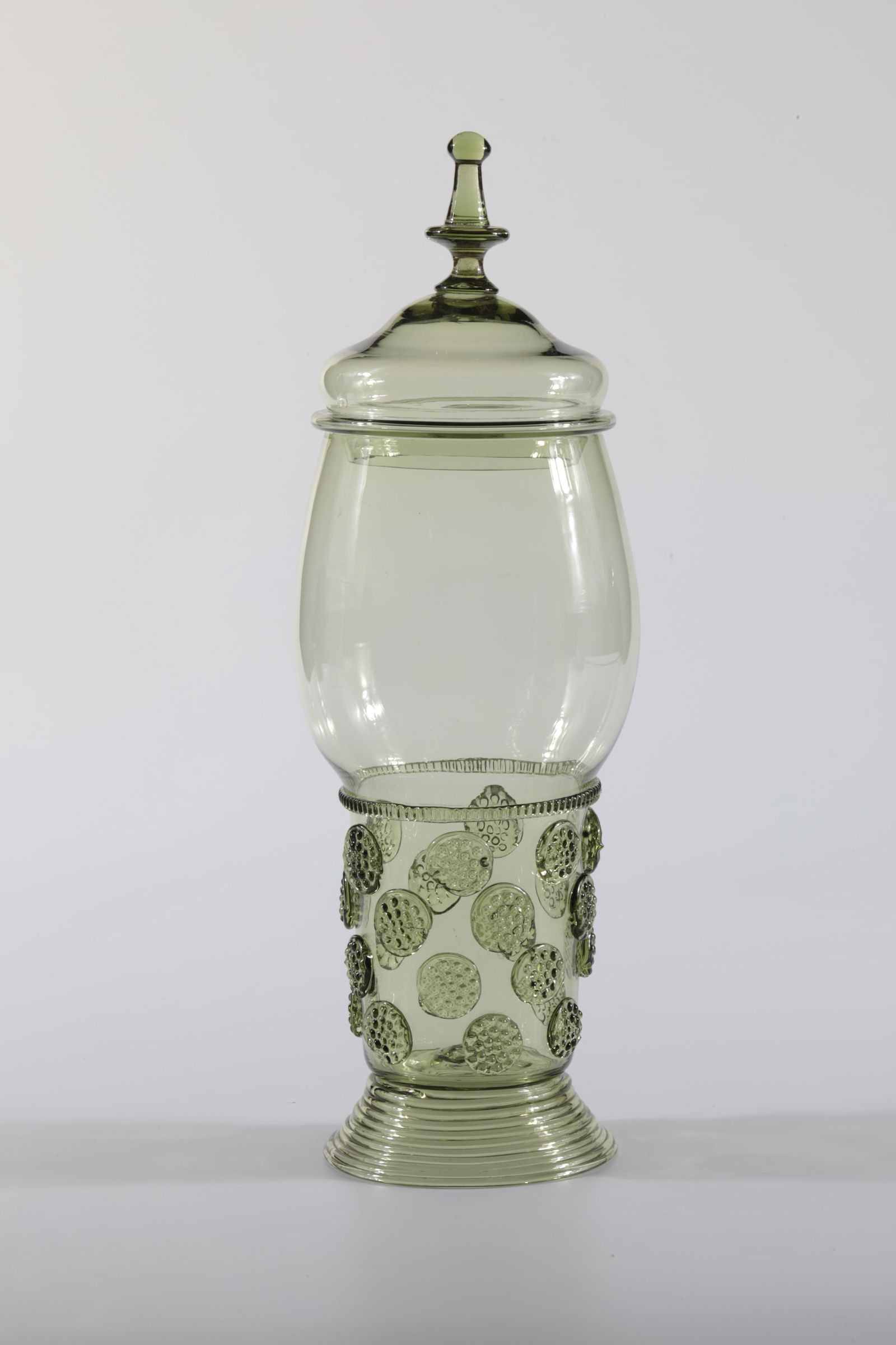 Merkens Cup with Lid: Merkens Goblet with lid Rheinische Glashütten AG, Cologne-Ehrenfeld, c. 1881 Olive-coloured glass. Braided foot, decorated with ribbed thread and nubs. H: 31 cm.