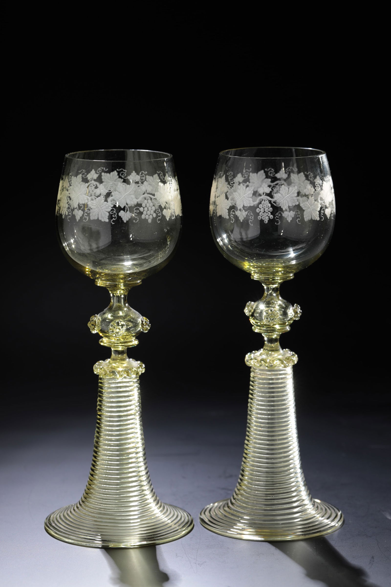 Two Romans Adolf: Two Römer Adolf Rheinische Glashütten AG, Cologne-Ehrenfeld, around 1881 Yellow-green glass. Vine tendrils engraved on kuppa, four nubs on nodus, foot spun. H: 20 cm.