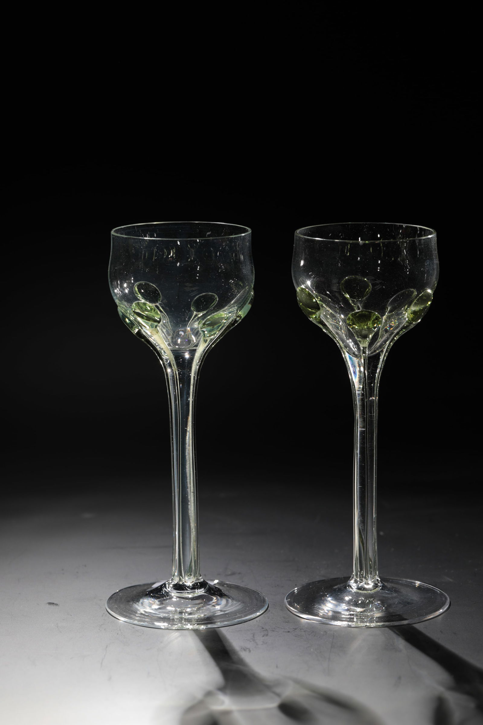 Two Madeira Romans: Two Madeira-Römer Rheinische Glashütten AG, Cologne-Ehrenfeld, around 1881 Colourless glass. Applied, elongated green drops from the tip end to the foot. H: 16.5 cm.