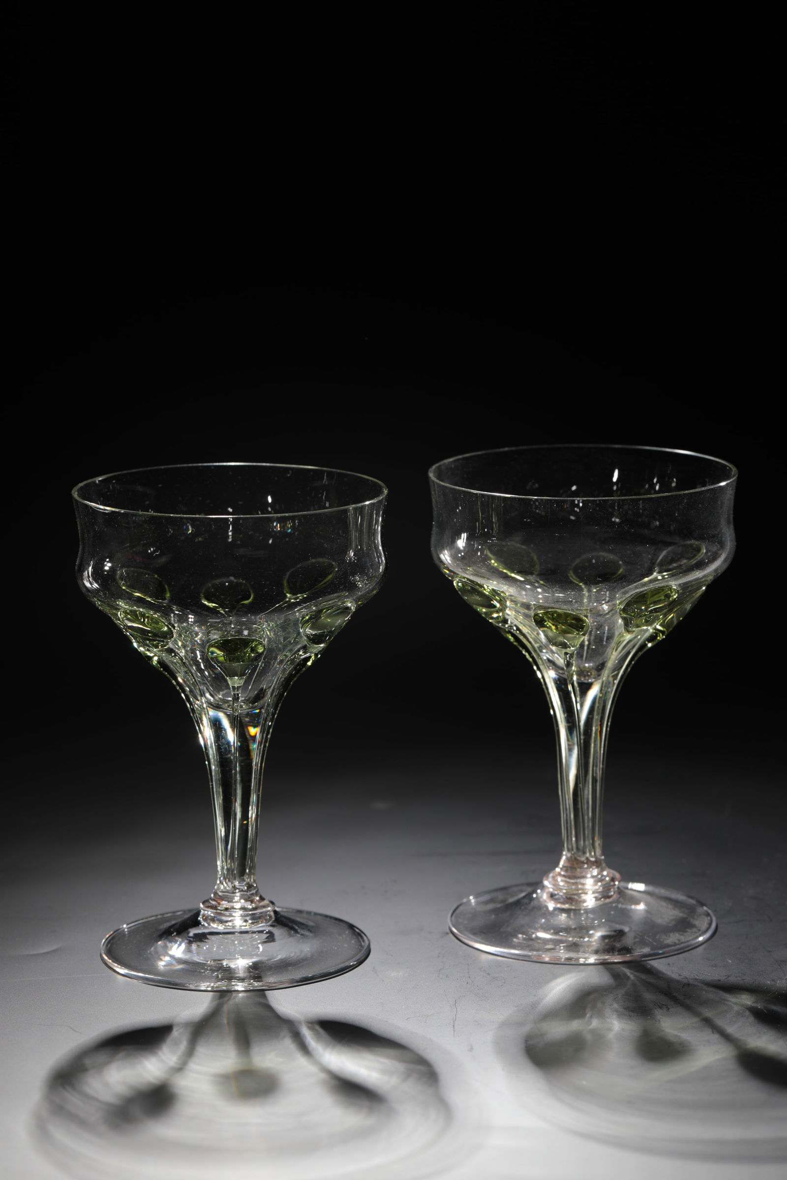 Two champagne bowls: Two champagne bowls Rheinische Glashütten AG, Cologne-Ehrenfeld, around 1881 Colourless glass with applied, elongated green drops from the tip end to the foot. H: 13.5 cm.