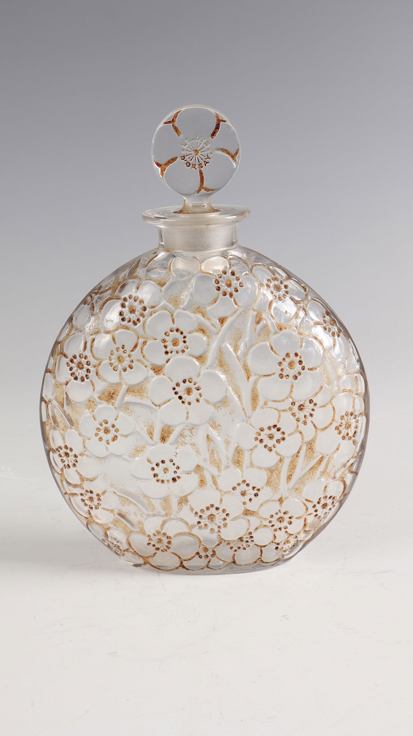 Bottle with stopper ''Le lys'': ottle with stopper ''Le lys'' René Lalique for d'Orsay, Wingen - sur - Moder, 1922 Colourless glass, moulded, refinished by polish, brown patina. Ref: R. LALIQUE (compression molded). H. 18.5 cm