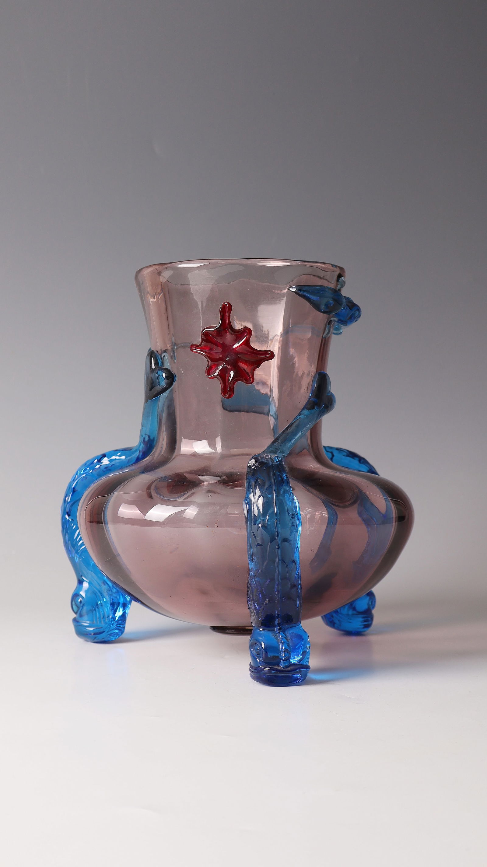 Vase with lizard and dolphin-shaped feet: Vase with lizard and dolphin-shaped feet Cristallerie de Sèvres, circa 1885 Amethyst-colored, optically blown glass with blue and red appliqués. H. 24.5 cm Lit.: G. Cappa, Le Genié Verrier de