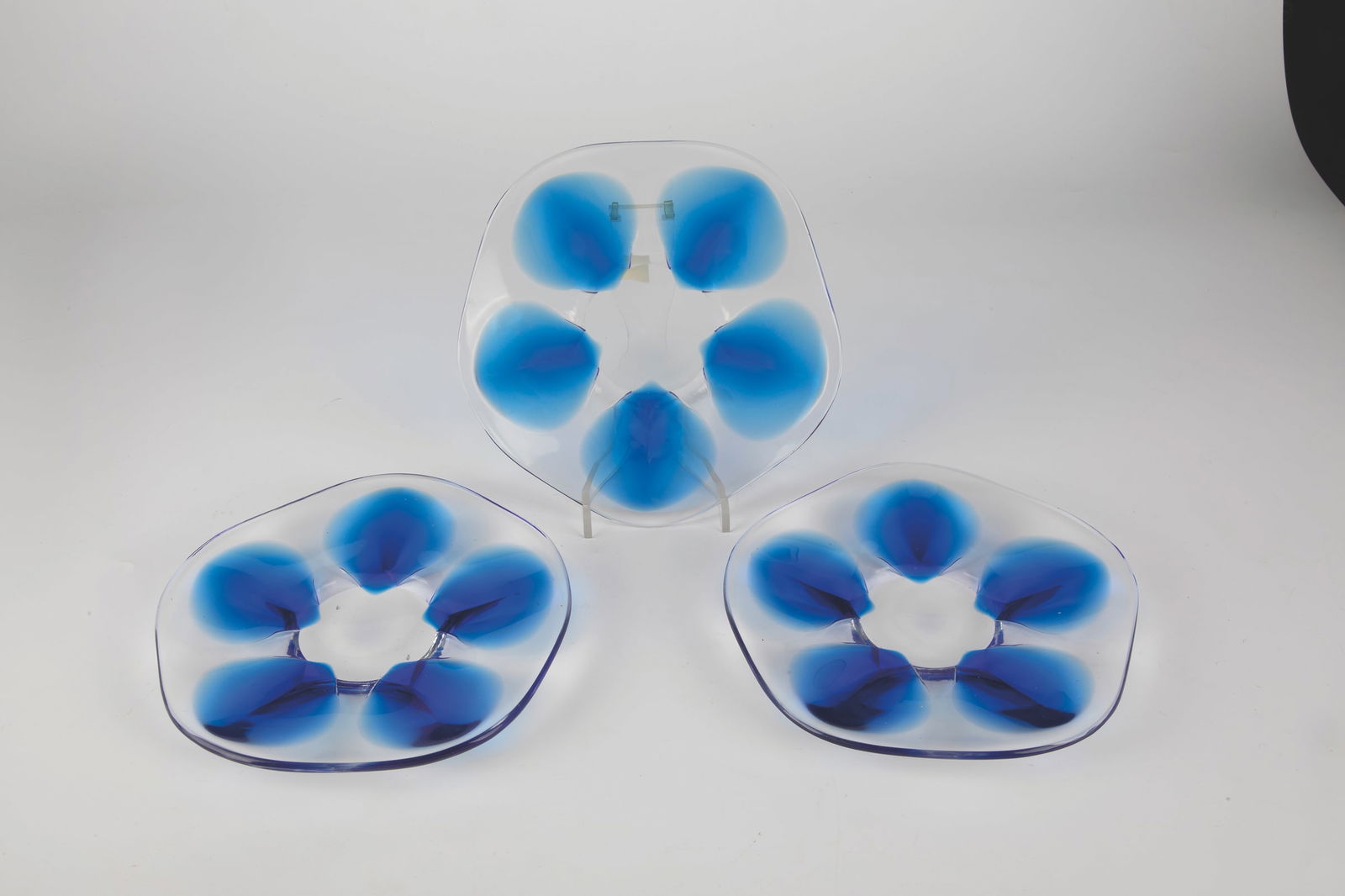Three plates: Three plates of Lalique, 20th century Colourless glass, each with five cobalt blue inclusions, which have been warped into stylised petals. Five-backed flag. On the ground in diamond crack inscribed: