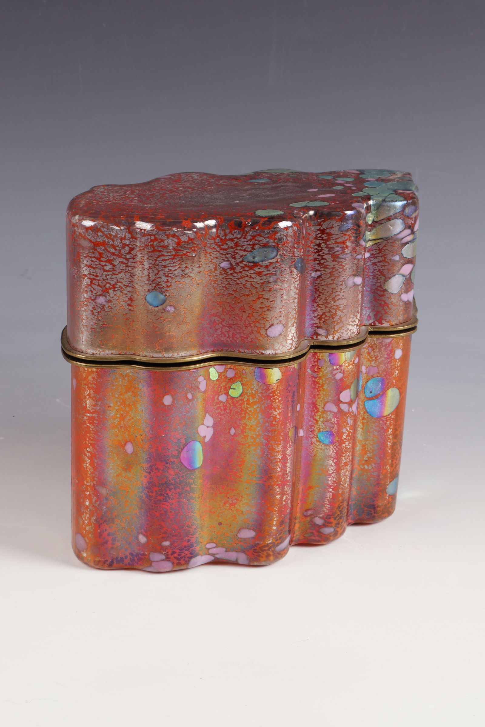 Lidded jar: Lidded box Jack Ink Colourless, thick-walled glass, with multi-coloured melting, strongly iridescent. Brass mount. In the bottom inscribed: Jack Ink 1227, H. 19 cm, L. 23 cm.