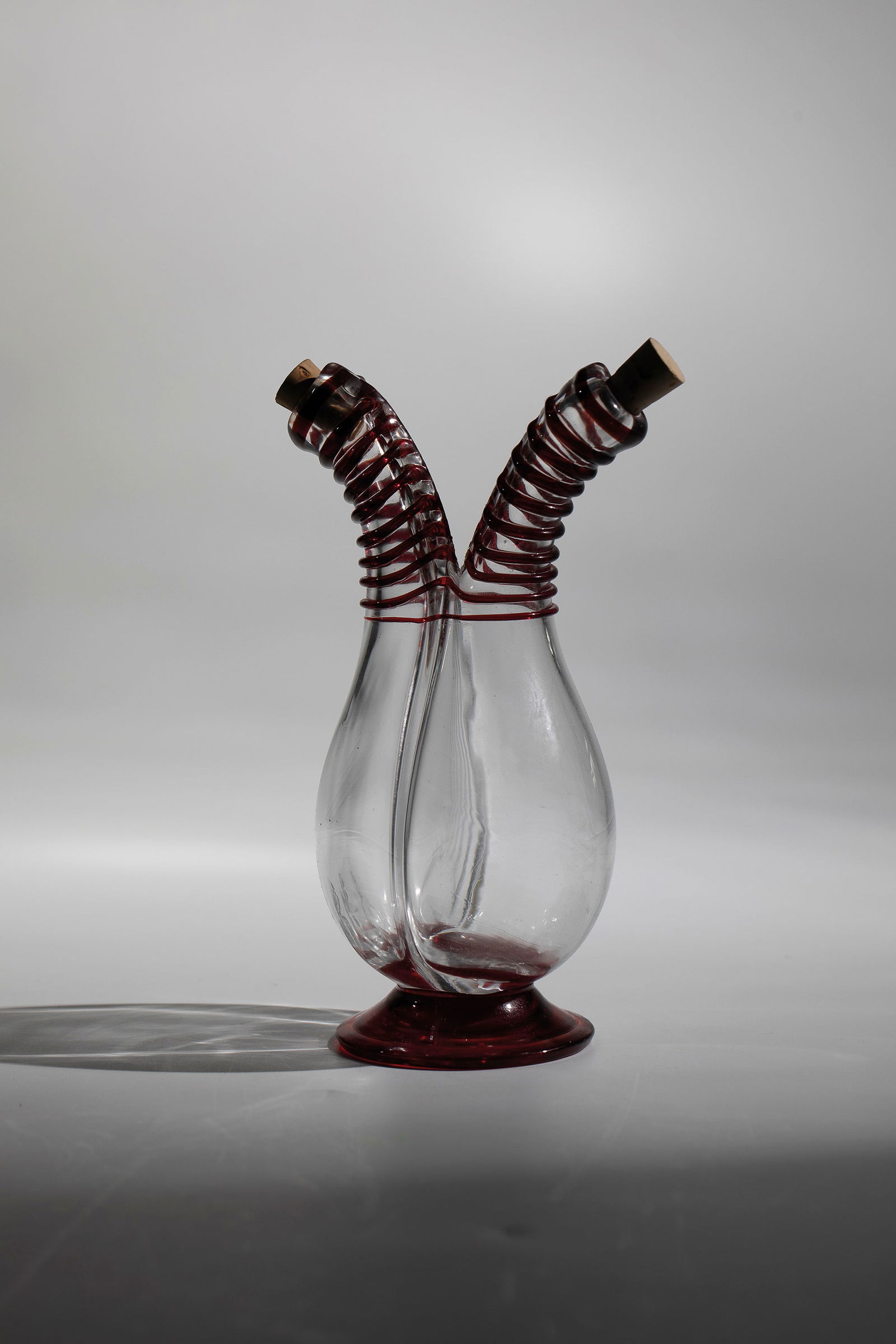 Vinegar & Oil Bottle: Vinegar and oil bottle Murano, early 20th century, colourless and red glass. Divided class body with two longitudinally optically drawn necks. Fused, ruby red glass thread décor. Cork stoppers. H.