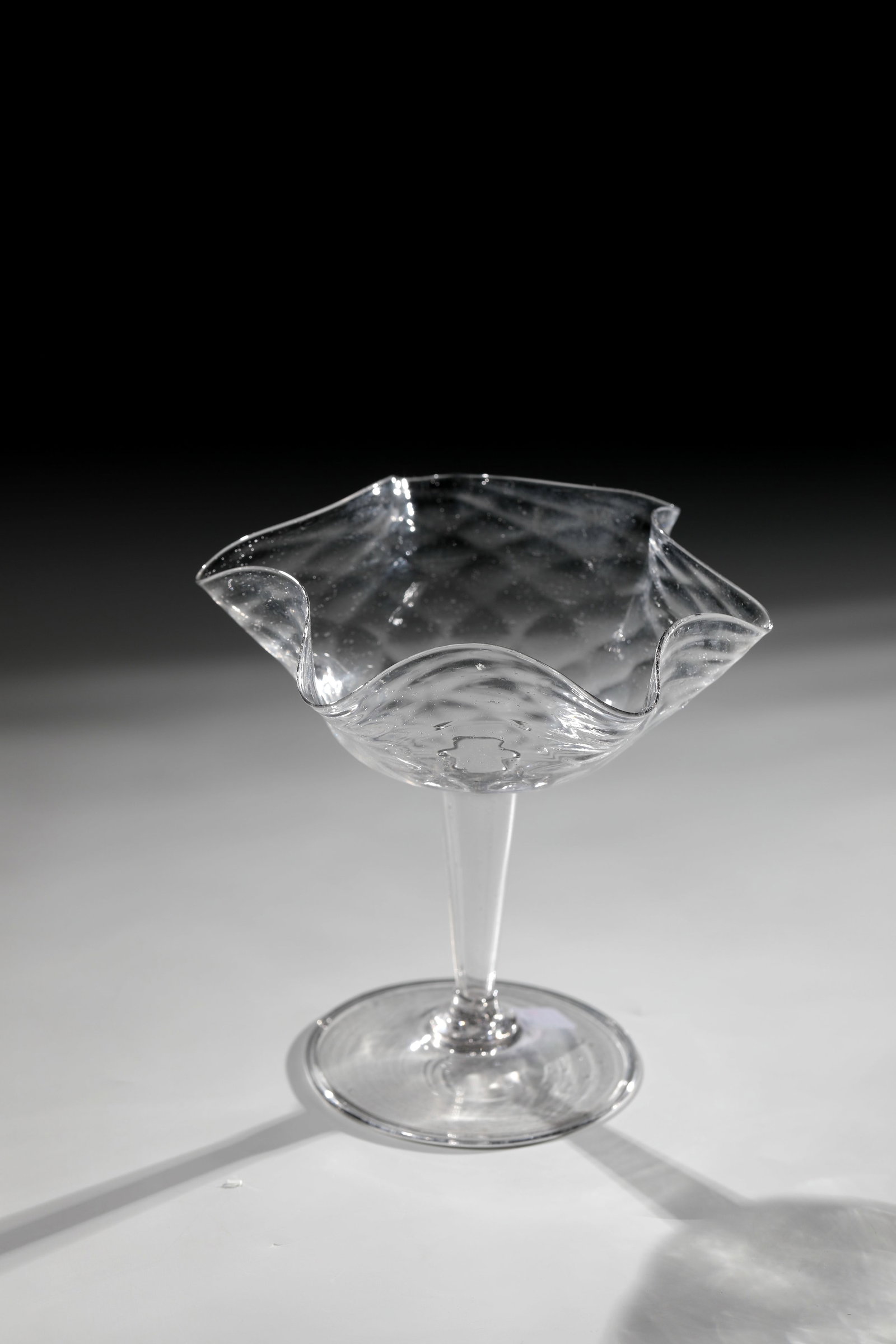 Small Tazza: Small Tazza Venice, 16th century Colourless, slightly greyish glass with fine tearing. Disc base with the edge folded downwards. Slightly conically widening hollow shaft. Kuppa with optical waffle dec