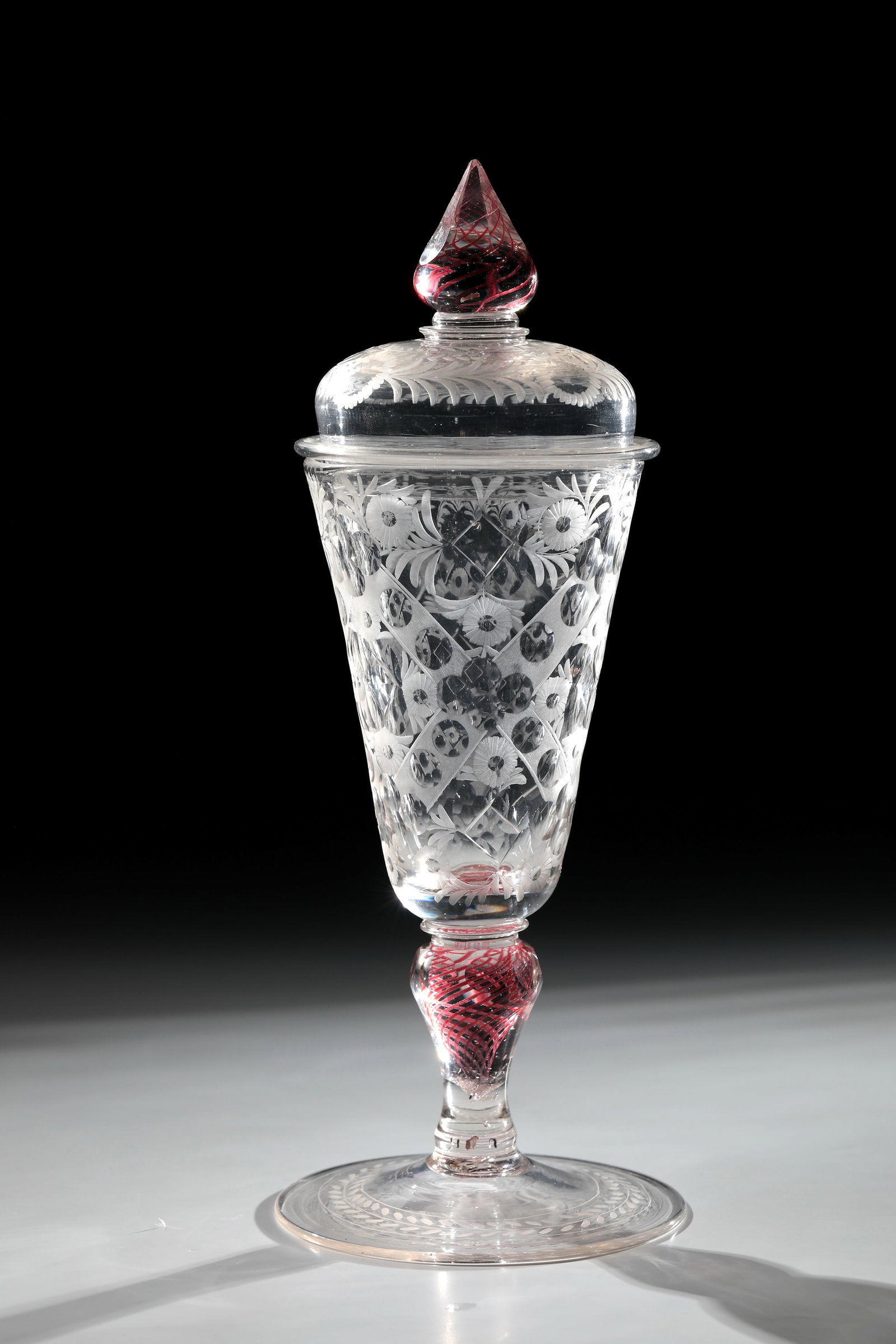 Lidded goblet with gold ruby threads: Lidded goblet with gold ruby threads Bohemia, A. 18th century, colourless glass. Disc base with tear and engraved leaf border on the upper side. Baluster shaft with spirally melted gold ruby threads