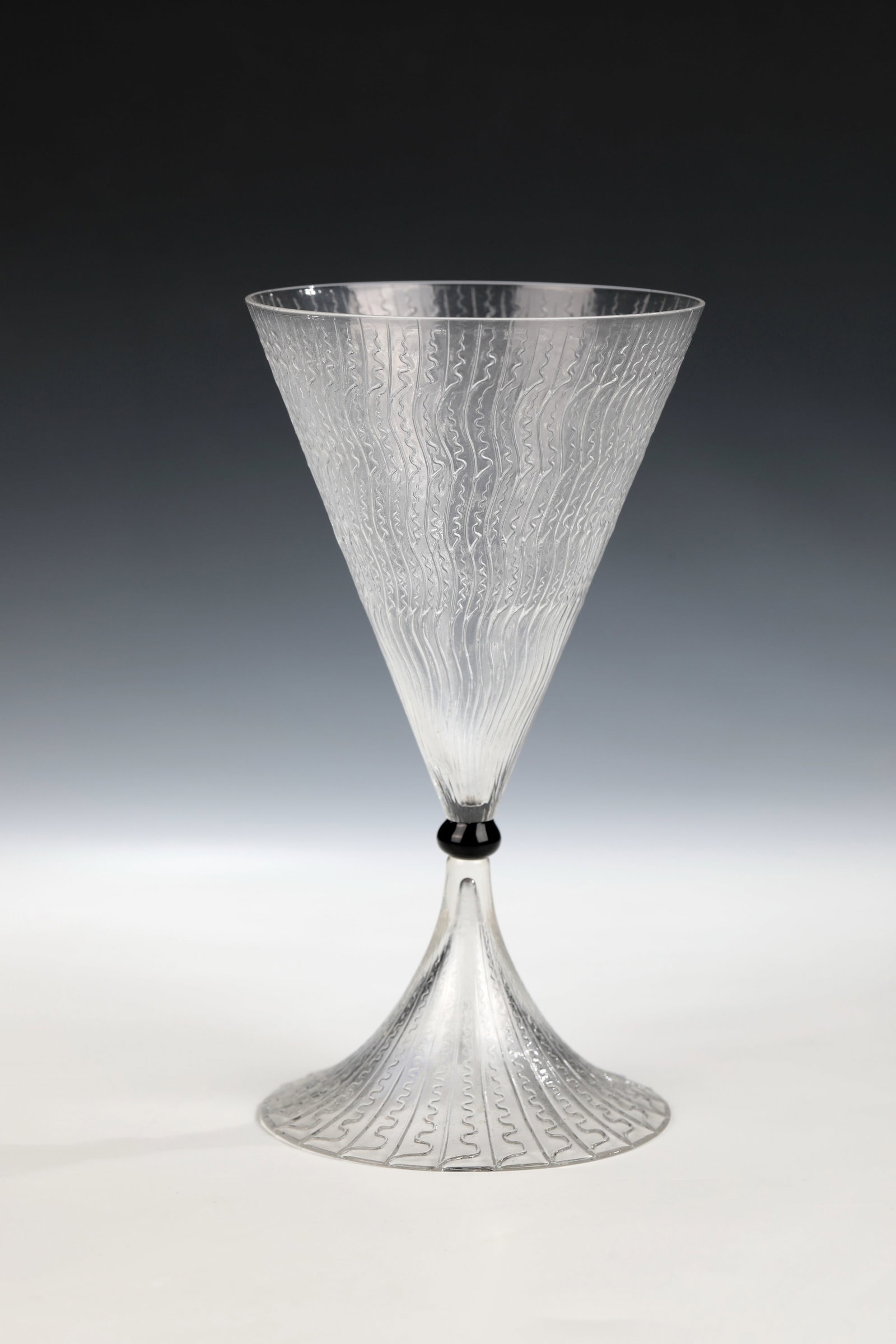 Drinking glass ''Vrilles de Vigne'': Drinking glass ''Vrilles de Vigne'' R. Lalique, Wingen-sur-Moder, 1921 Colourless glass, pressed into the mould, as well as nodus made of black glass. Relief décor: waves and lines. Bottom may refer 