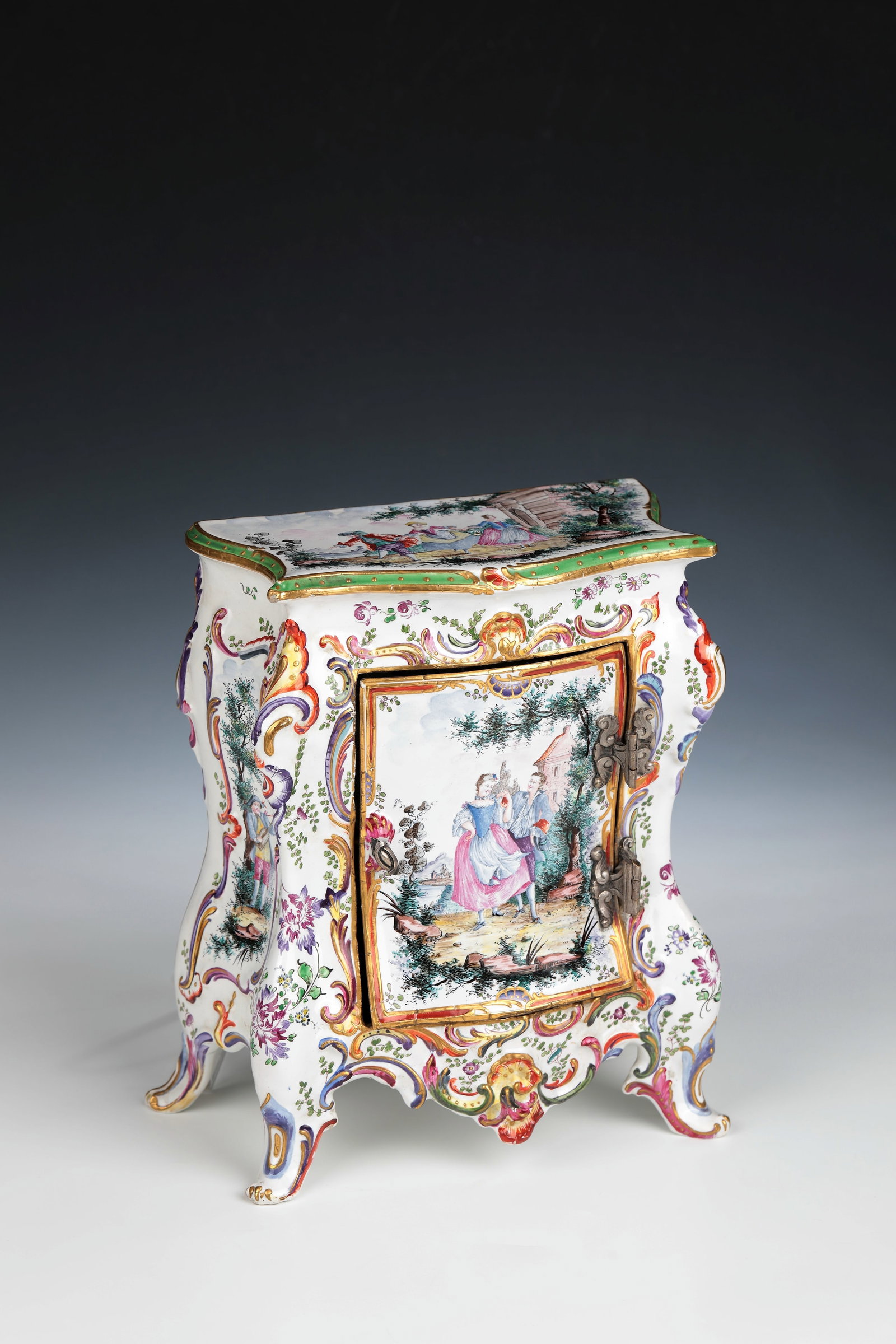 Faience chest of drawers: Faience chest of drawers France, 19th century In cross-section, rectangular body with three curved sides, standing on four volute feet, frontally a door with iron hinges. Polychrome, partly gold-heigh