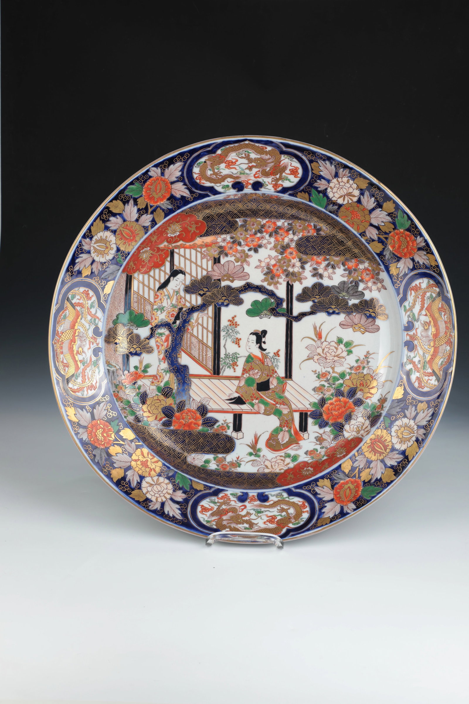 Large-format, heavy-walled Imari panel: Large-format, heavy-walled Imari plate Arita, Japan, probably 19th century porcelain with polychrome, area-filling hand and gold painting. In the mirror, two geishas in a garden setting. The flag