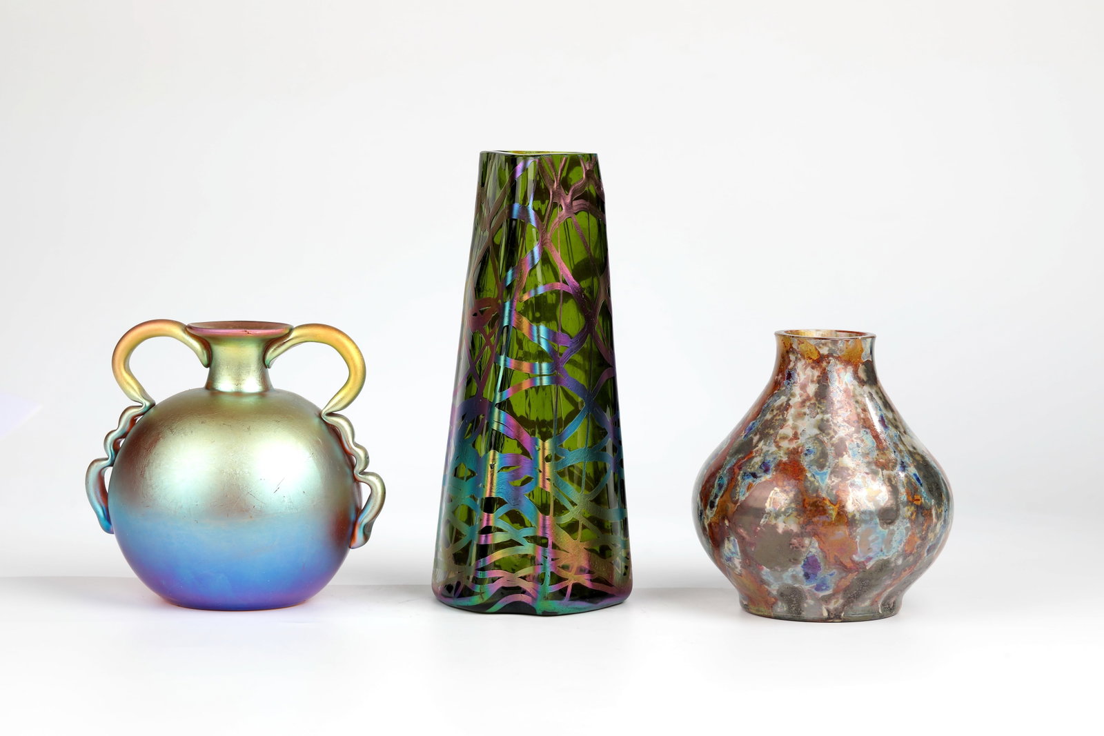 Three Vases: Three vases including WMF, Geislingen, around 1930 Colourless glass, silvery-blue-violet-yellow-gold iridescent. Two freely applied handles. h. 12.5 cm; vase: Josef Knizek, Antonienhütte glass