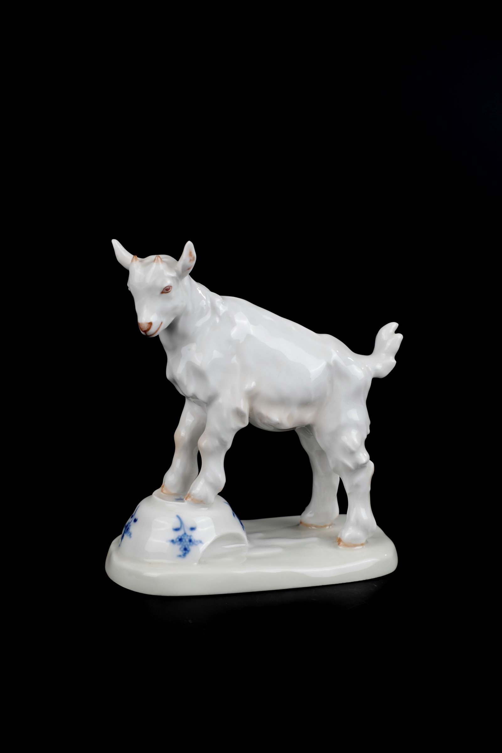 Kid goat: Kid designed by Erich Hösel, Meissen, 2nd half of the 20th century Above an oval base, with both front feet standing on a damaged Altmeissen dish-bowl, a kid goat. Economical underglaze