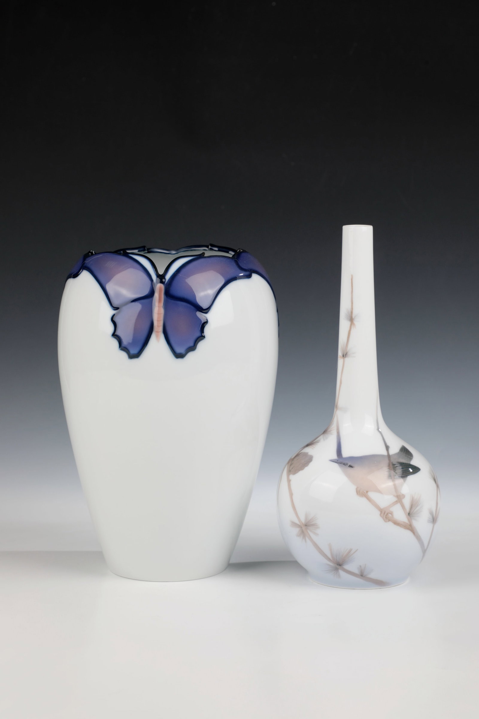 Two vases: Two vases Royal Copenhagen, c. 1900 / 1923 Vase with three butterflies in relief at the edge of the mouth. Manufactory brand, form no. 899. H. 24 cm. Long-necked vase with on pine branch. H. 25 cm.