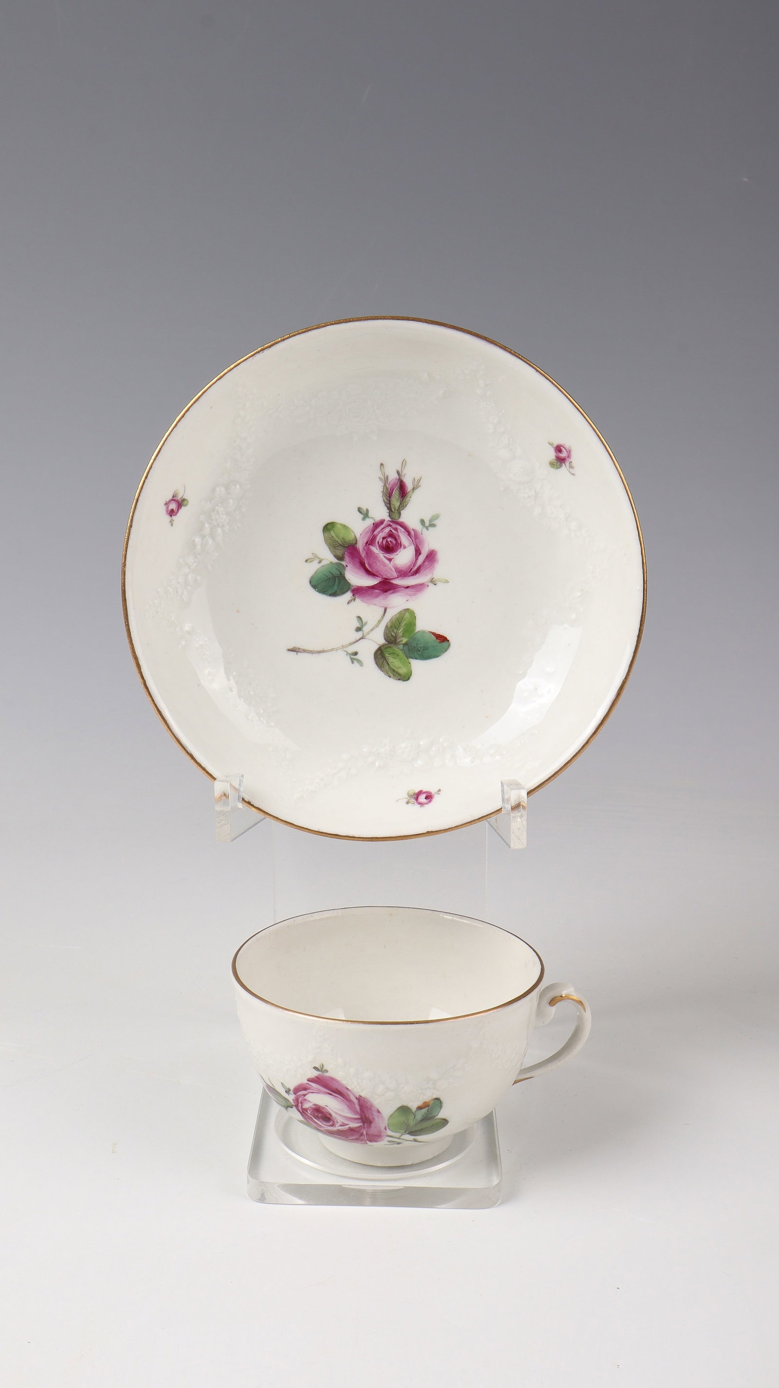 Cup and saucer: Cup and saucer designed by Gottfried Riedel, Ludwigsburg around 1765 With raised flower garland relief and rose decoration. Gold rim. Blue manufactory brand. H. 6 cm, D. 12.7 cm.