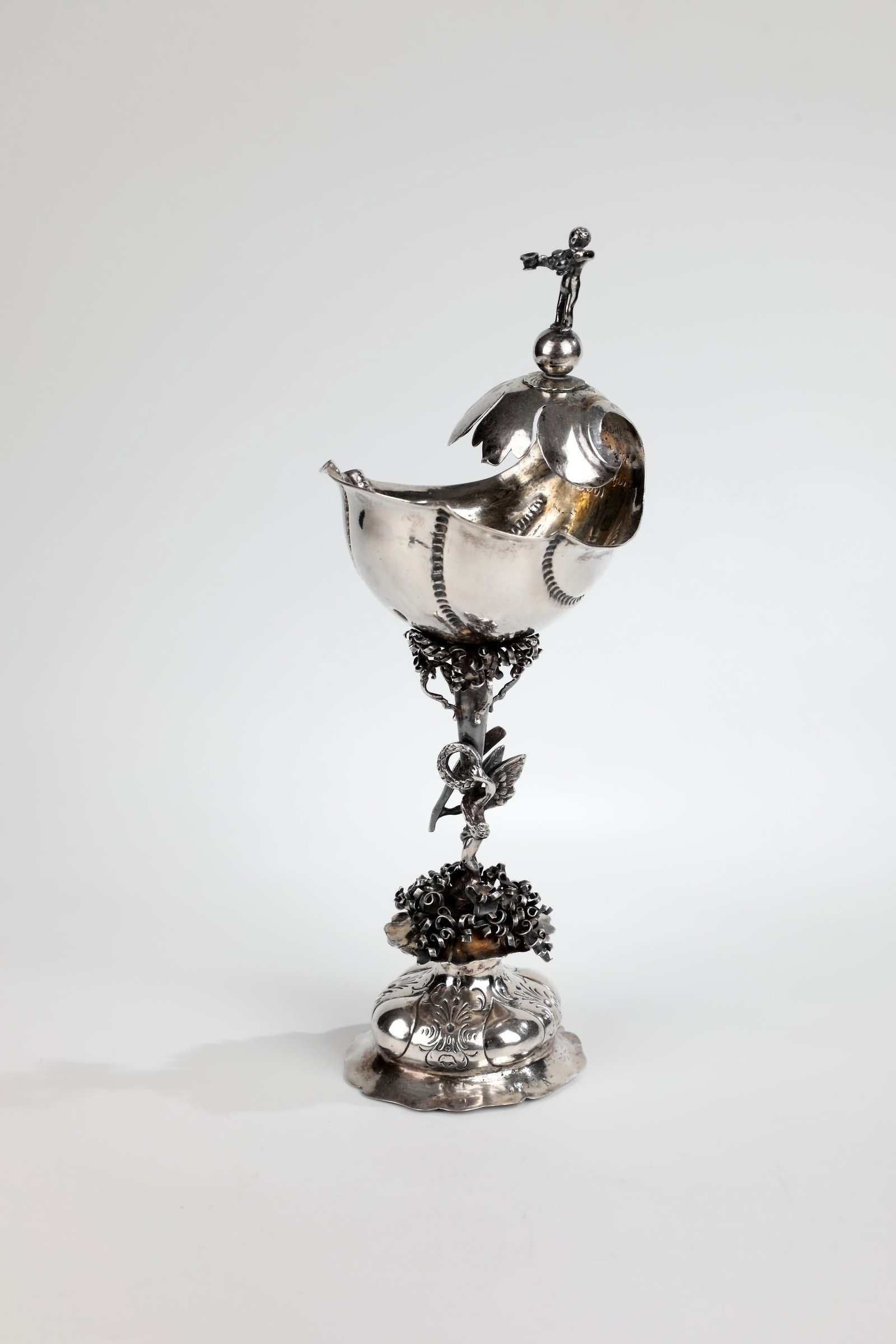 Shell cup: Shell goblet German, 19th century Silver embossed, cast and engraved. On a fourfold humped foot a genius with palm branch and laurel wreath as a shaft figure. The shell-shaped cuppa crowned by a
