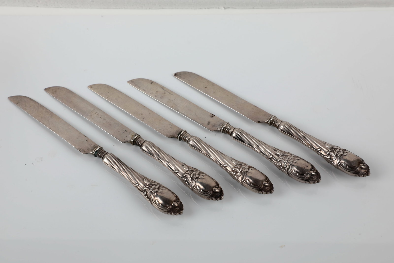 Five dessert knives: Five dessert knives Russia, c. 1900 silver. Handles with relief decoration of curly leaf and flower motifs and twisted barrel. Stamped with fineness ''84'' and indistinct master's mark. L. 17 cm. 184 