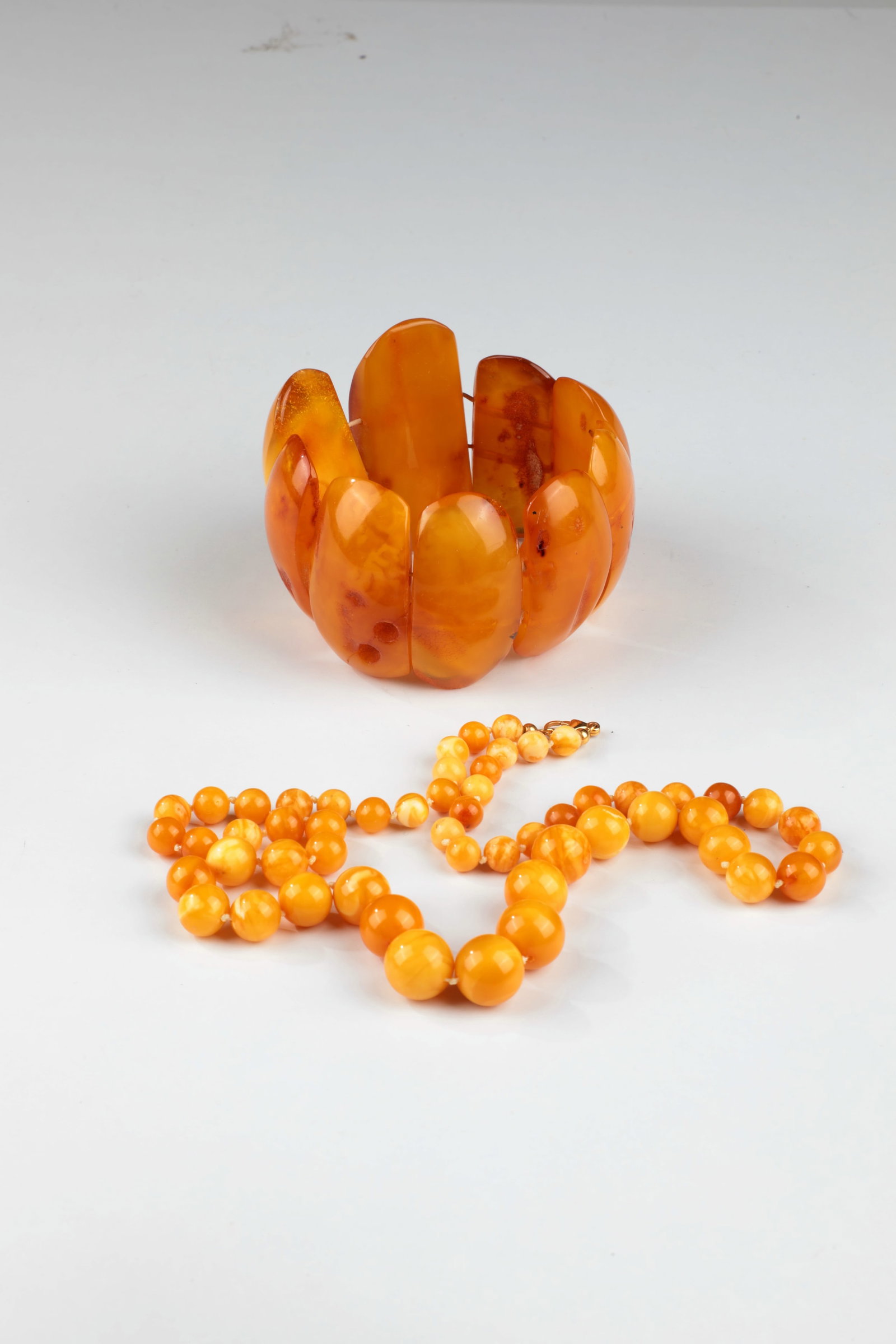 Butterscotch Amber, 2 parts: Butterscotch amber, 2 pieces Consisting of a necklace made of individually knotted amber balls in various sizes, with metal clasp and lobster clasp, as well as a solid bracelet with flat, wide amber
