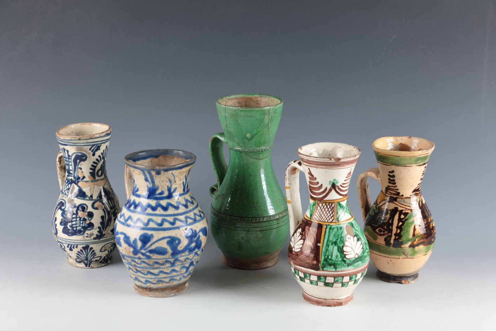 Mixed lot of five pear jugs: Mixed lot of five pear jugs Transylvania, 19th century Four with colourful or coblate blue floral décor on an ivory background, one with green glaze and ribbed rings. Restored, partly damaged.