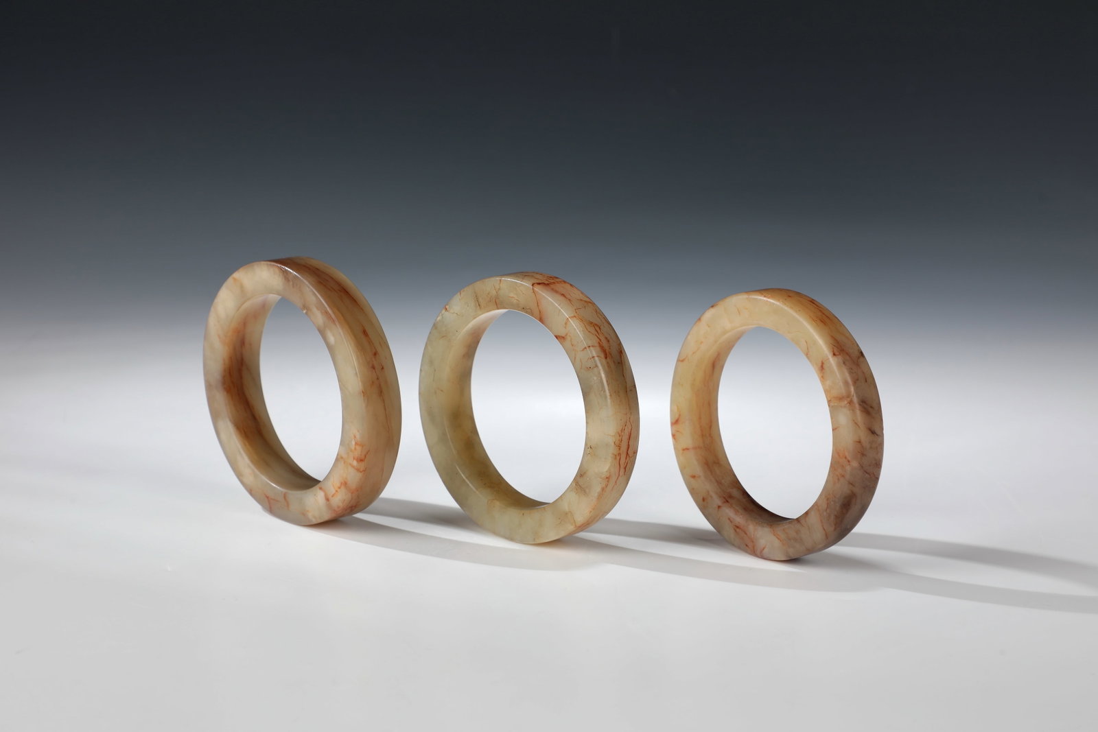 Three solid jade bangles: Three solid bangles made of jade China, 20th/ 21st century Mixed lot of three solid jade bangles with reddish-brown-beige inclusions and natural grain. Partially ground or rubbed. Inner diameter