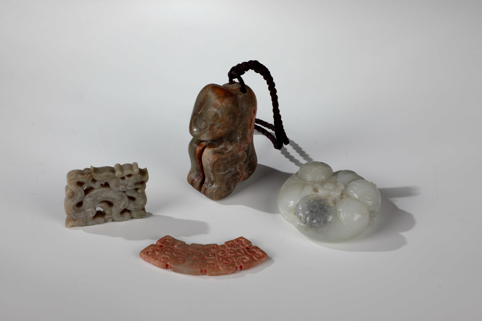 Mixed Lot of Various Jade Carvings: Mixed lot of various jade carvings China, around 1900 Mixed lot of four jade carvings, including various pendants and amulets. Bow-shaped huang pendant with engraved cloud pattern, dragon pendant,