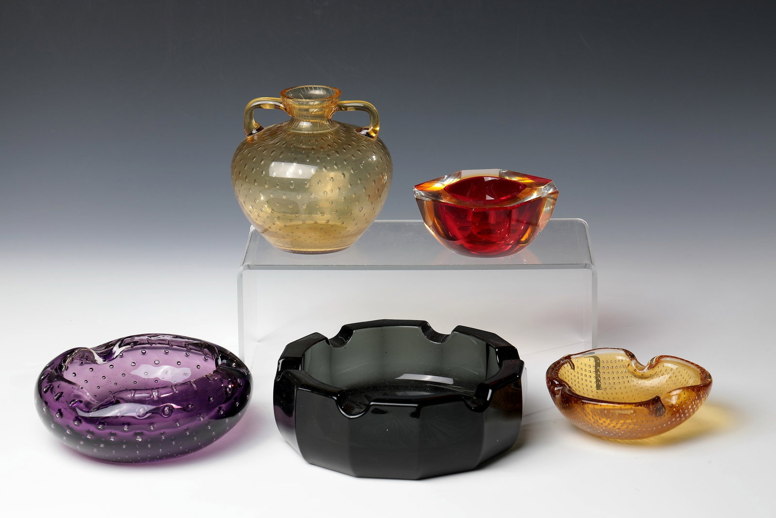 Mixed lot of four ashtrays and a vase with handles: Mixed lot of four ashtrays and a handle vase Murano, 1950s/60s Honey-yellow glass and colourless glass with red and magenta underlays and pierced air bubbles. D. 11.5 cm; 14.5 cm; 15 cm.'' Konvolut