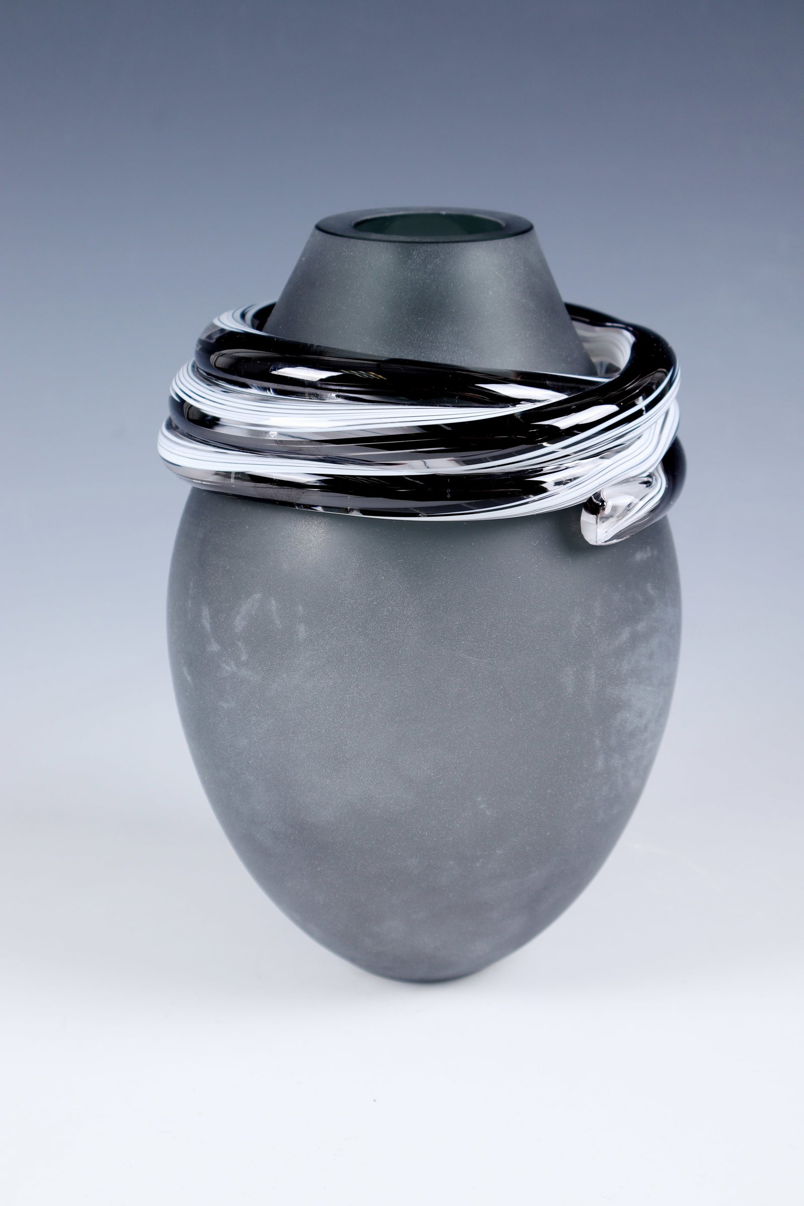 Vase ''Brasa Colorosa'': Vase ''Brasa Colorosa'' Melvin Anderson (design), Nový Bor, 2008 Smoky grey glass, frosted outer wall. Below the muzzle edge, multi-fold application made of colourless glass with white and
