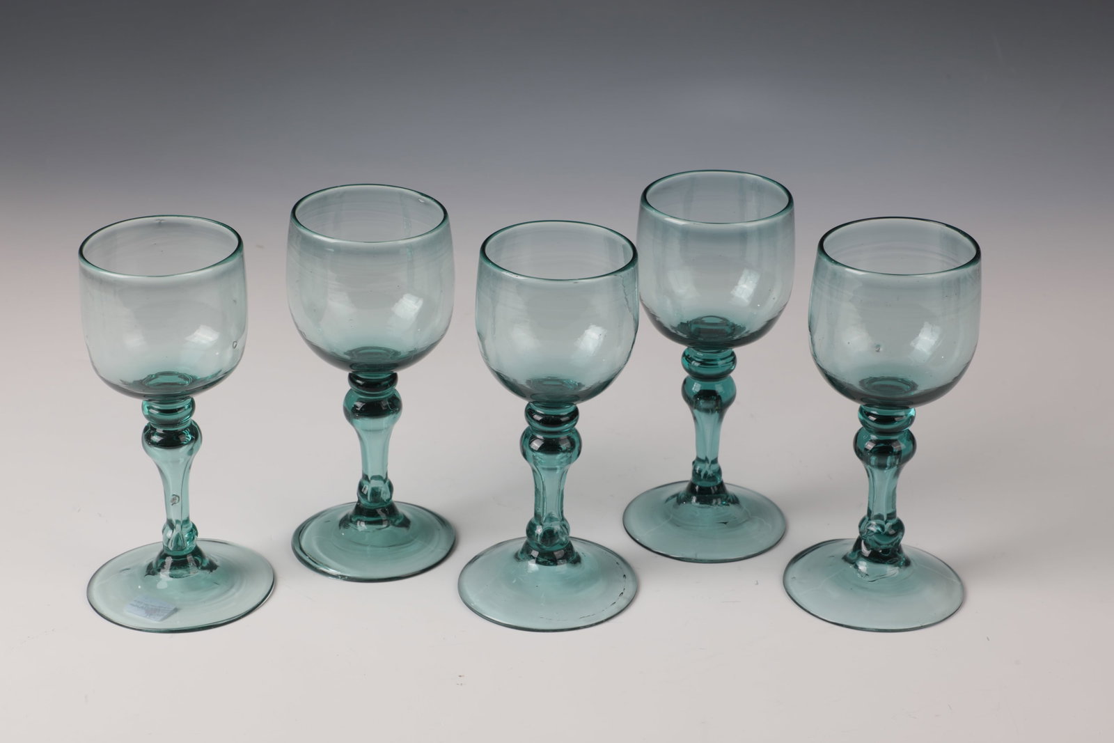 Five Romans: Five Romans England, E. 19th century. Light green glass with tear-off. Disc base, hollow baluster shaft with spherical nodus and bulbous cup. H. 15.5 cm Fünf Römer England, E. 19. Jh.