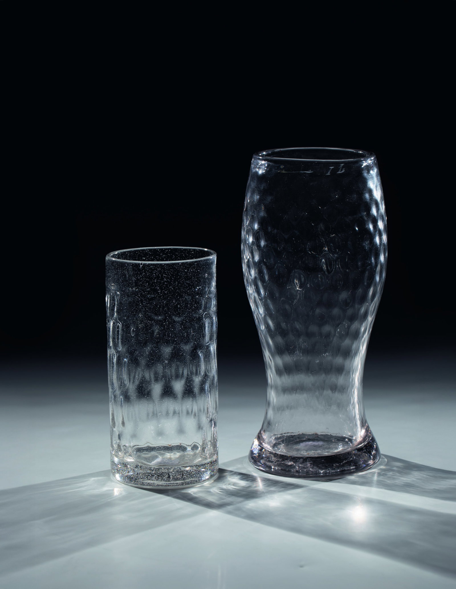 Club cups and rod cups: Club cup and rod cup South German, 19th century Colourless glass with tear-off and optical wrestling decoration. Club cup with engraved calibration line ''1L''. H. 15.5 or 22 cm Keulenbecher und